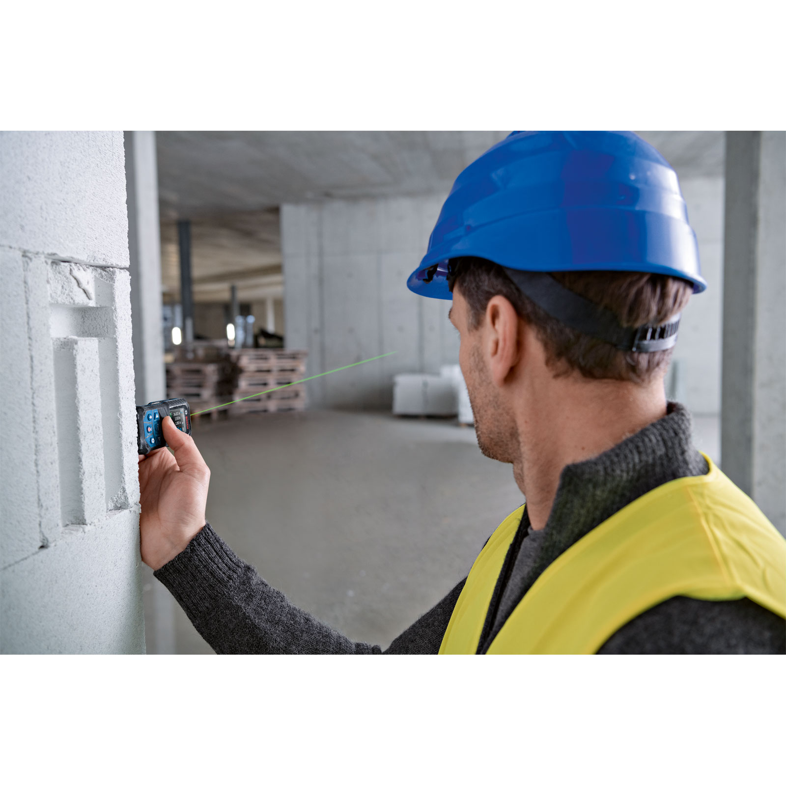 Un operaio edile utilizza un misuratore laser Bosch su un muro bianco in un edificio.
