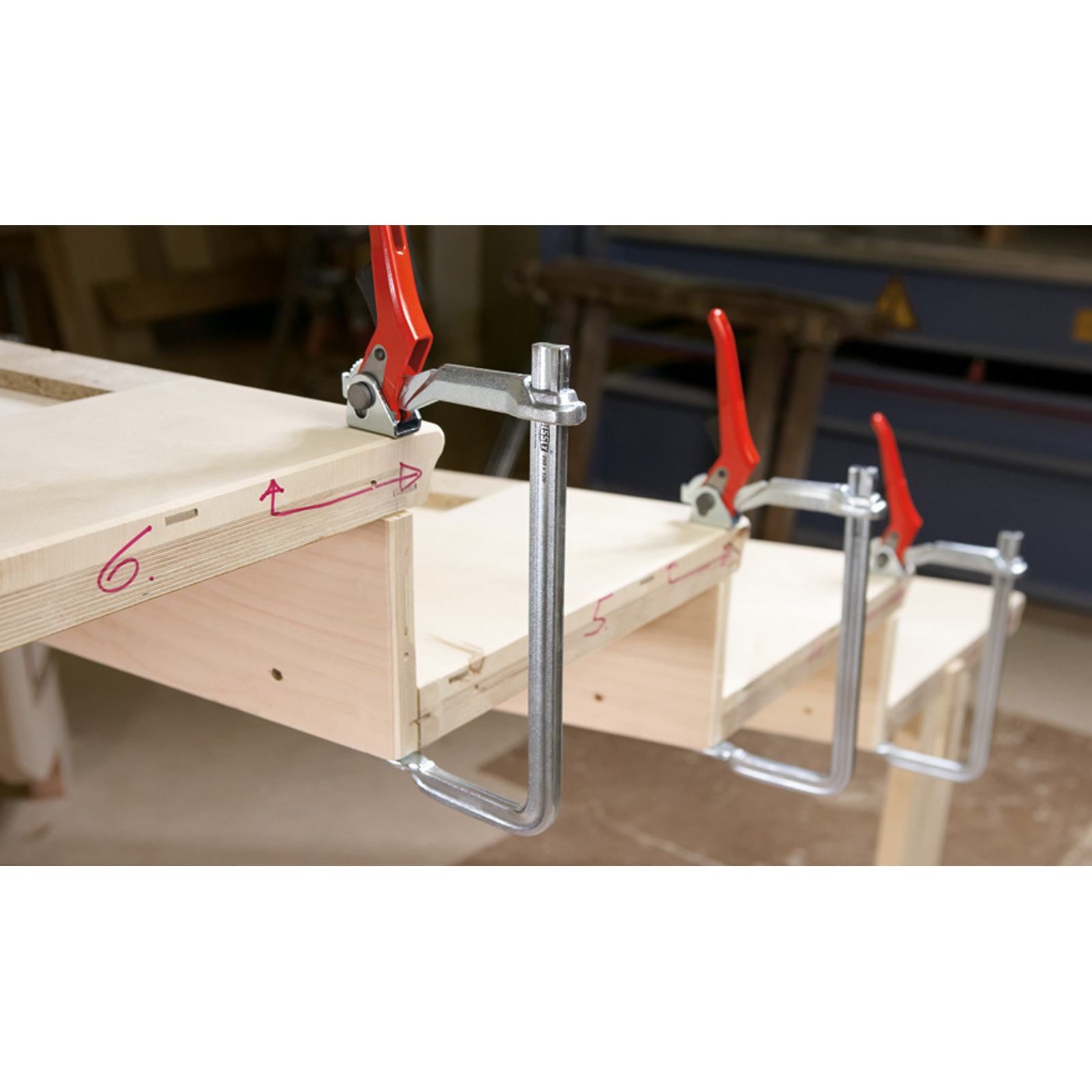 Holzteile mit roten und silbernen Klemmen auf einer Werkbank zusammengeklemmt.