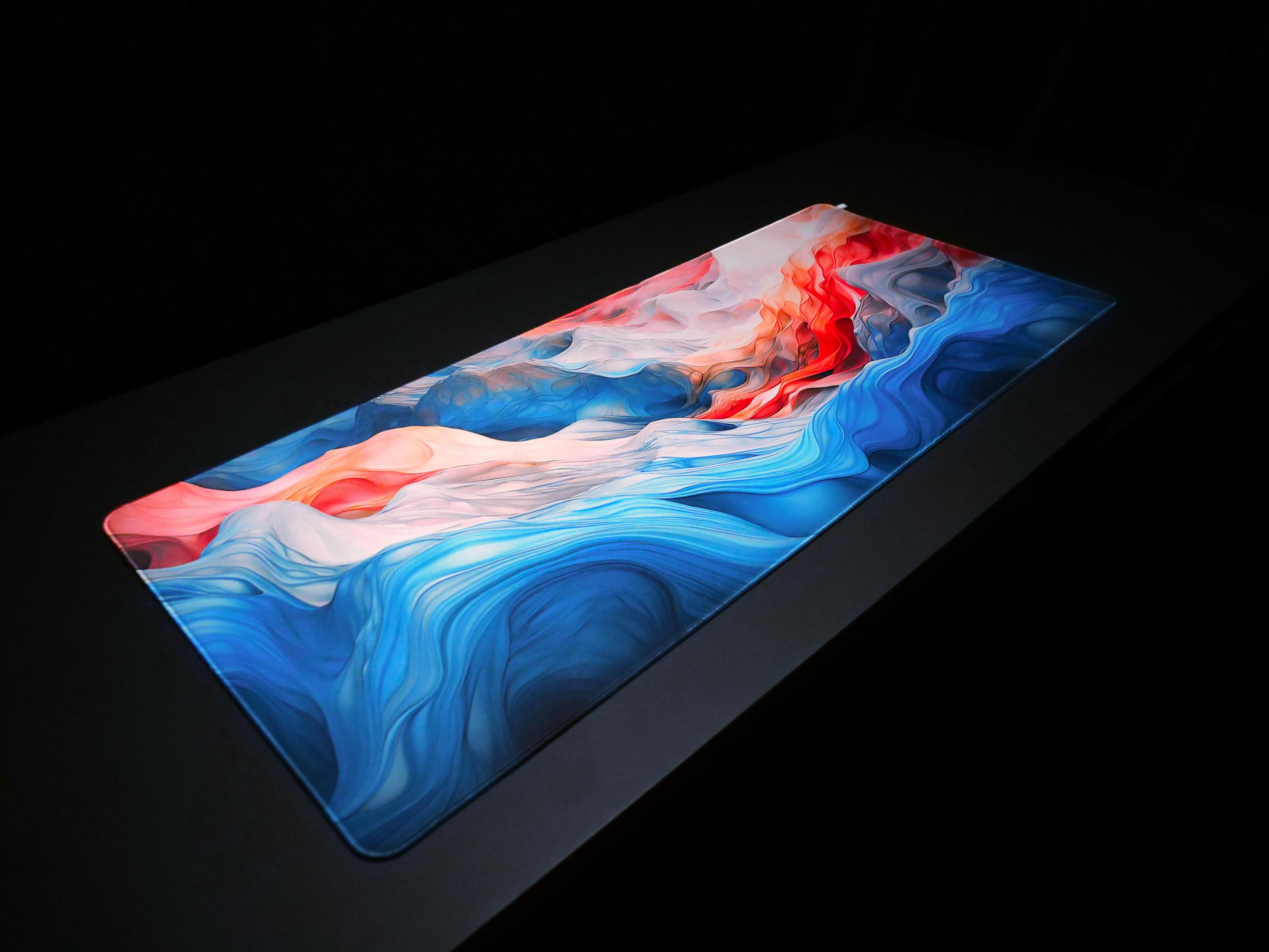 Un tapis de souris avec des motifs abstraits bleus, blancs et rouges sur une table noire.