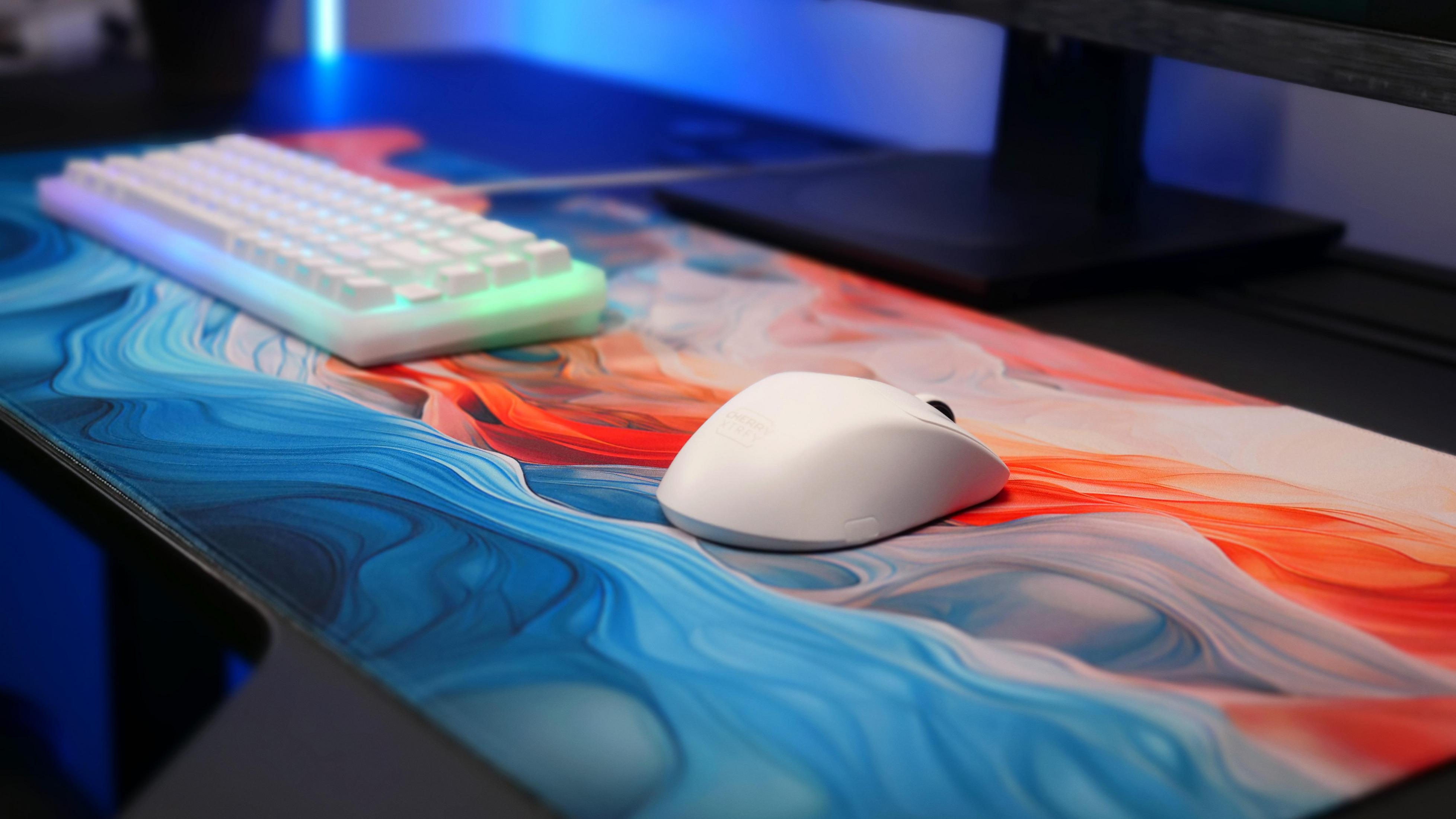 Une souris blanche et un clavier blanc sur un tapis de souris abstrait bleu, orange et blanc.