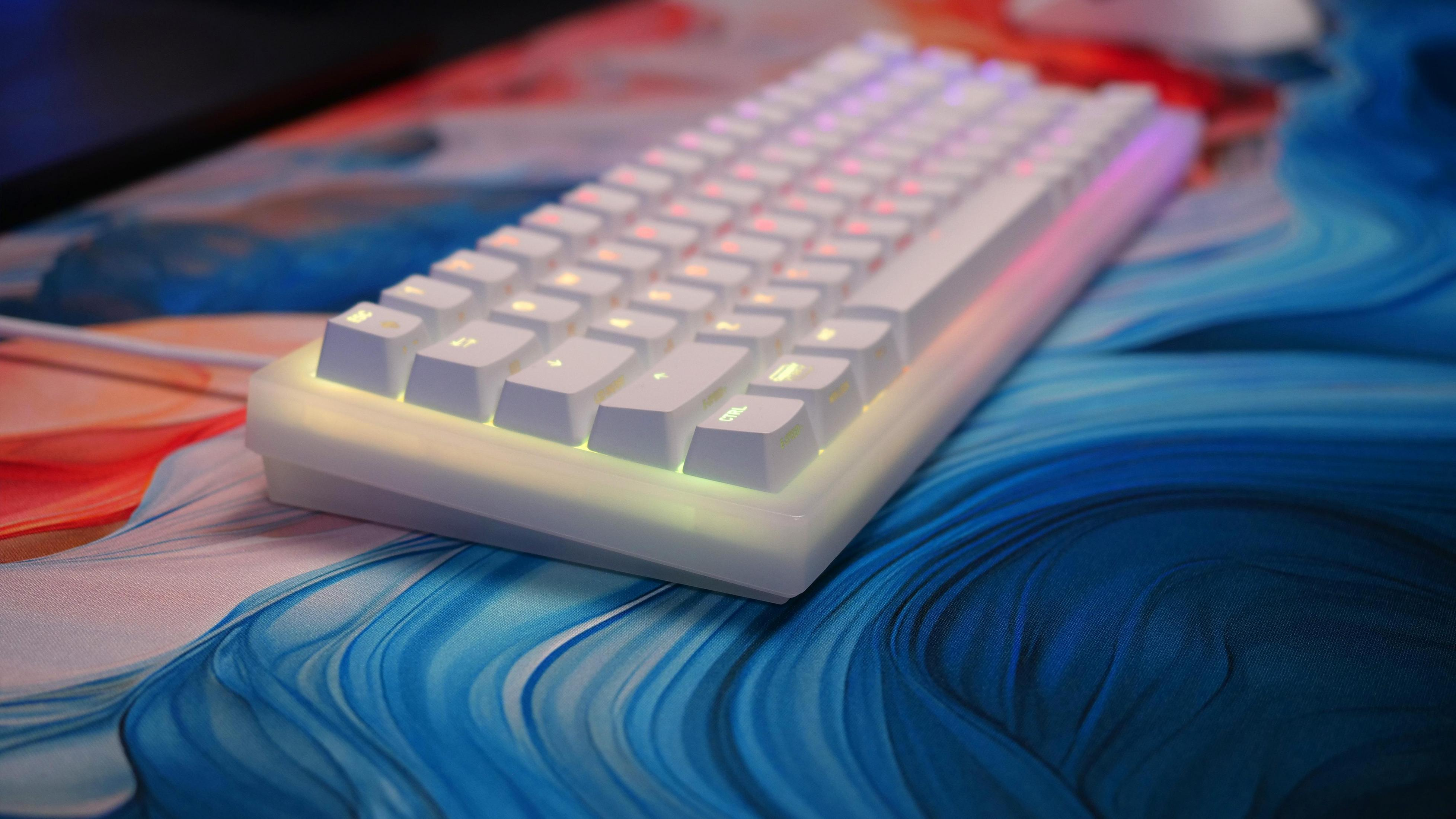 Un clavier blanc avec un éclairage arc-en-ciel sur un tapis de souris abstrait bleu, orange et blanc.
