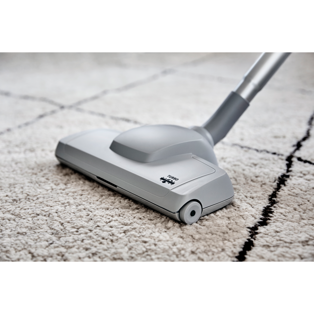 Tête d'aspirateur grise sur un tapis blanc avec des lignes noires sur fond noir.