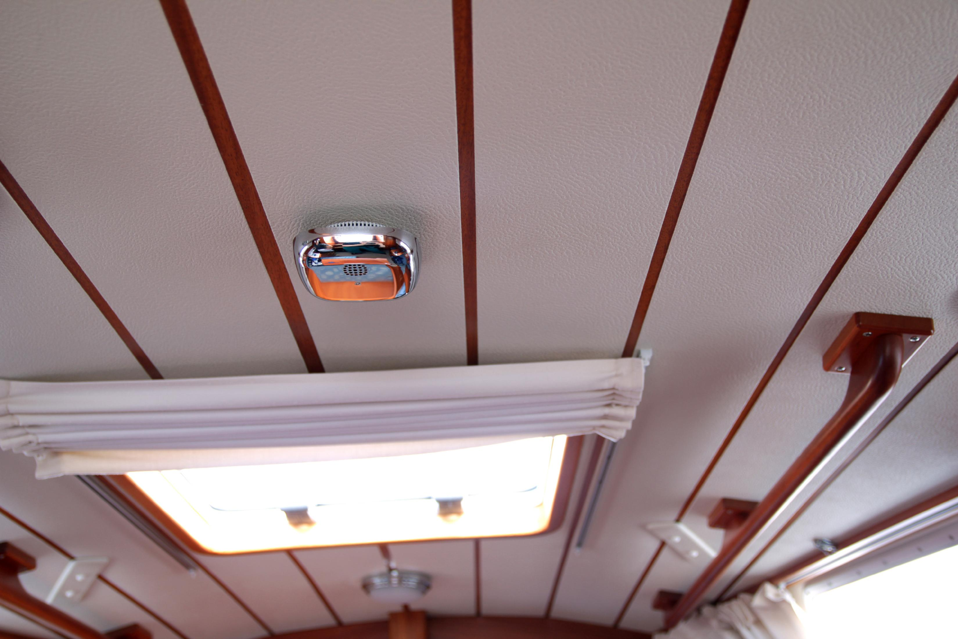 Ein Rauchmelder an einer Decke mit Holzplanken und einem Oberlicht im Hintergrund.