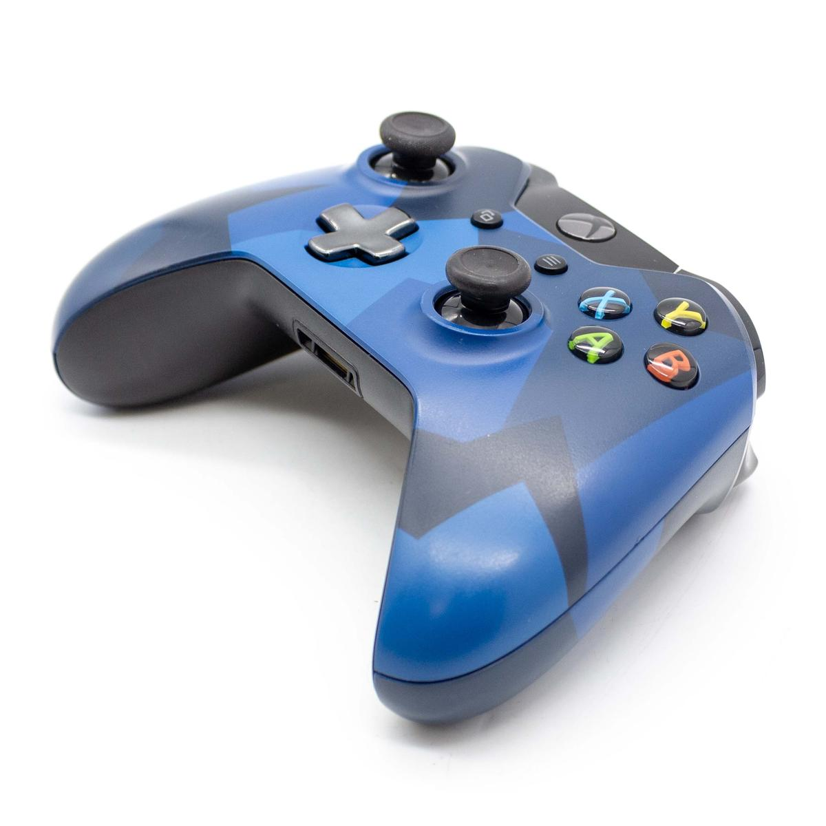 Ein blauer Xbox-Controller mit Tarnmuster liegt auf einer weißen Oberfläche, aus einem niedrigen Winkel betrachtet.