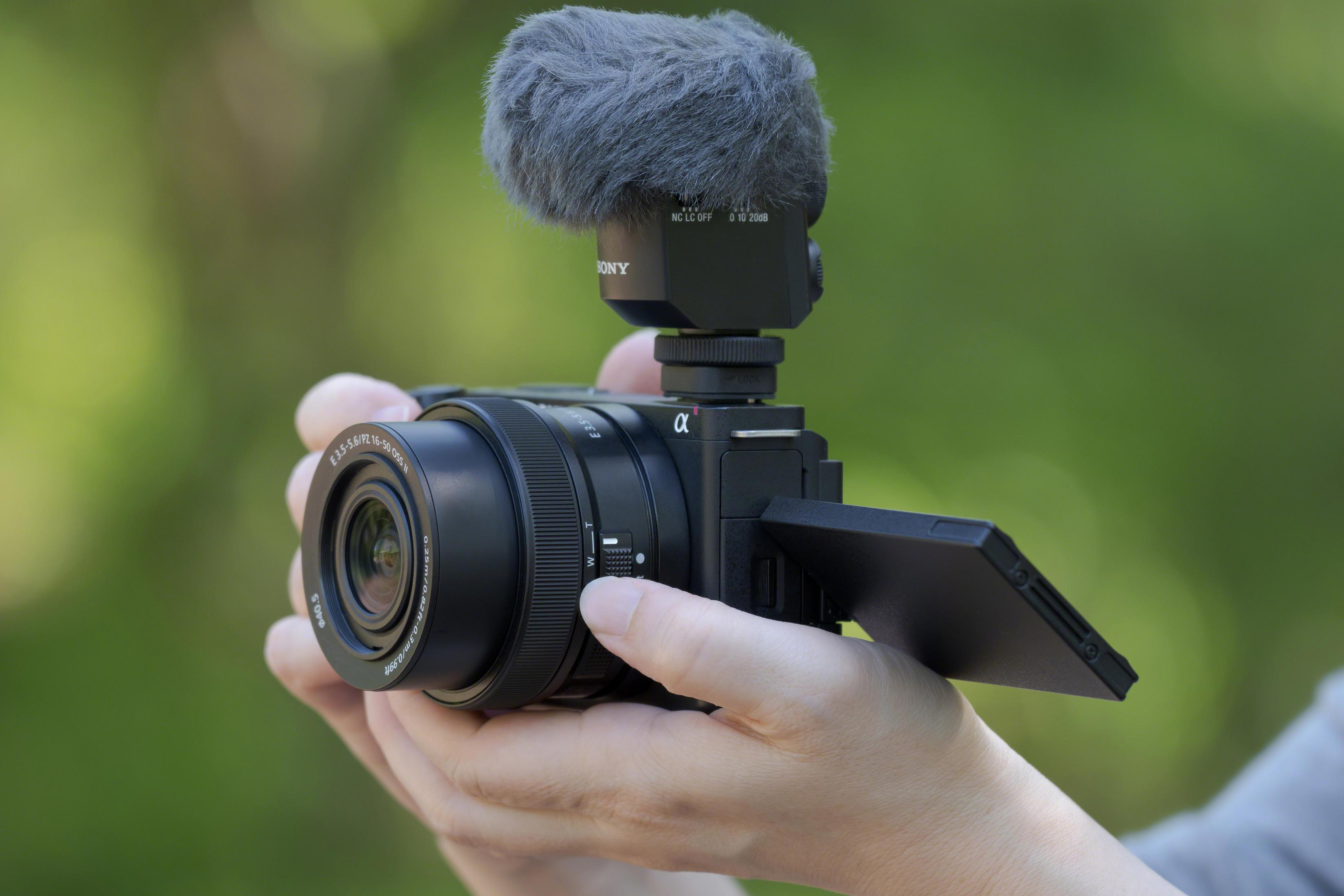 Hände halten eine Sony-Kamera mit Mikrofon und ausklappbarem Bildschirm.
