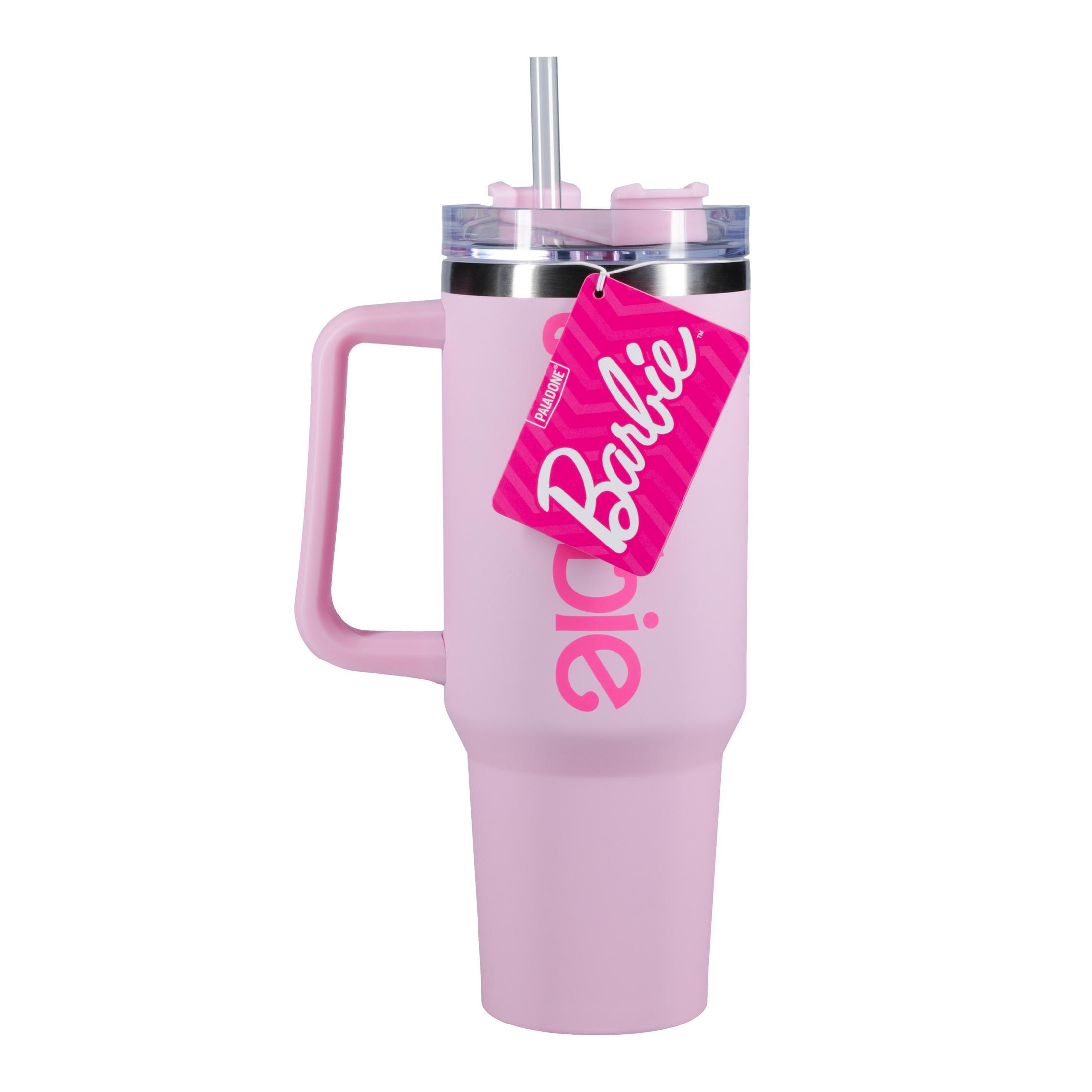 Un vaso de color rosa claro con un asa y una tapa transparente con una pajita. El nombre Barbie está escrito en él con una etiqueta.