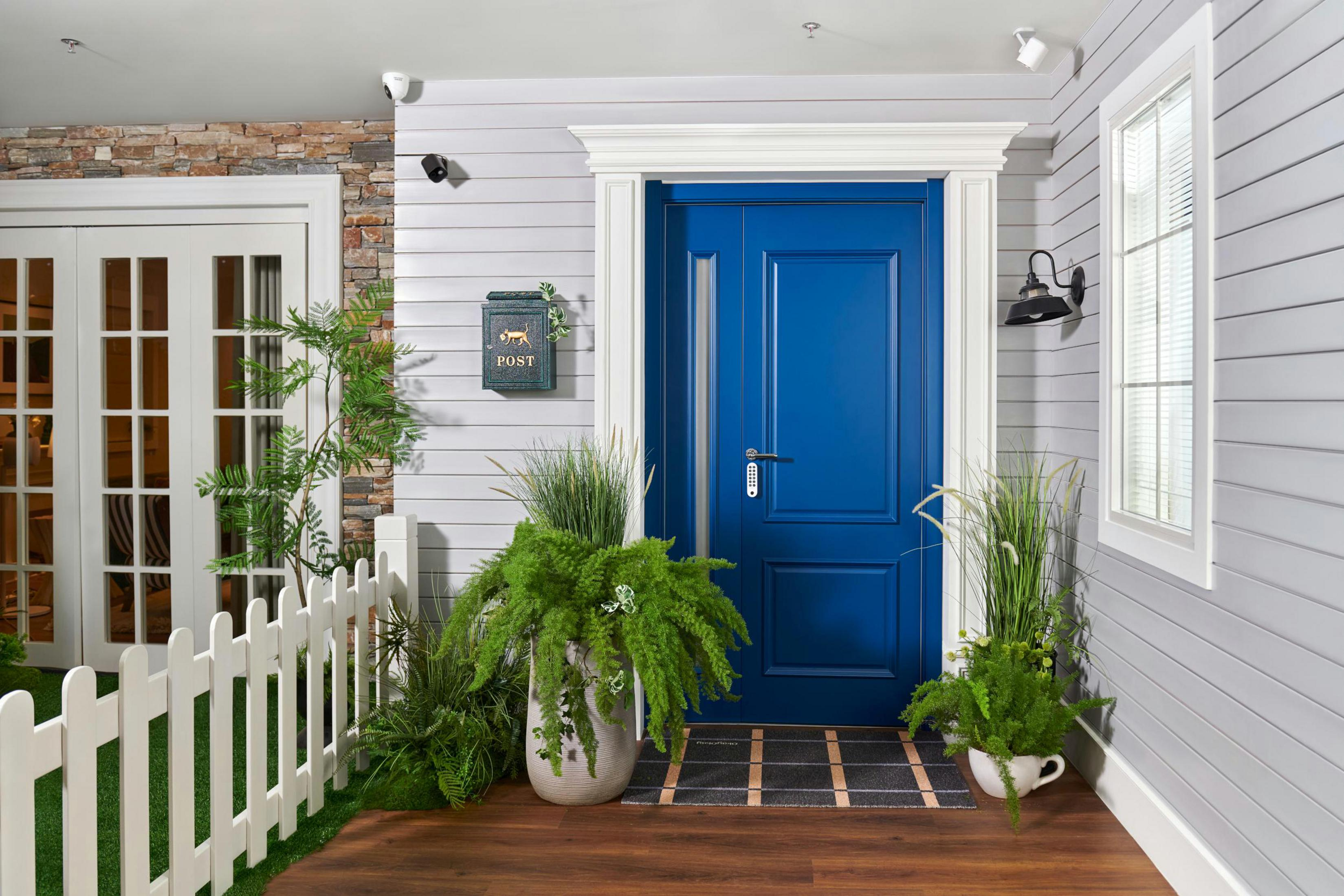Una porta blu è incorniciata da un rivestimento bianco, con due telecamere di sicurezza sopra e piante davanti alla porta.