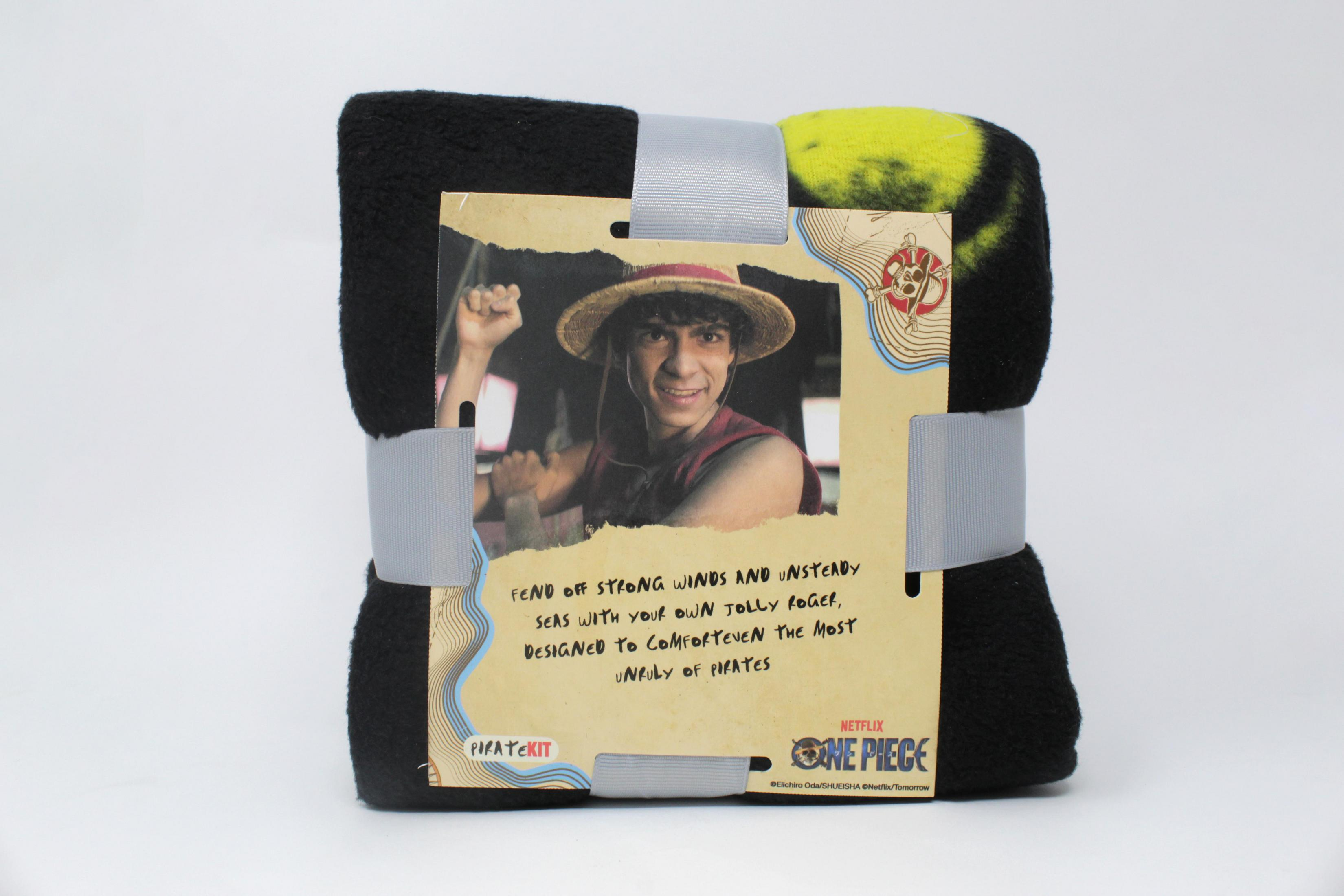 Eine gefaltete schwarze One Piece Decke, verpackt mit einem Foto einer Figur mit Strohhut.