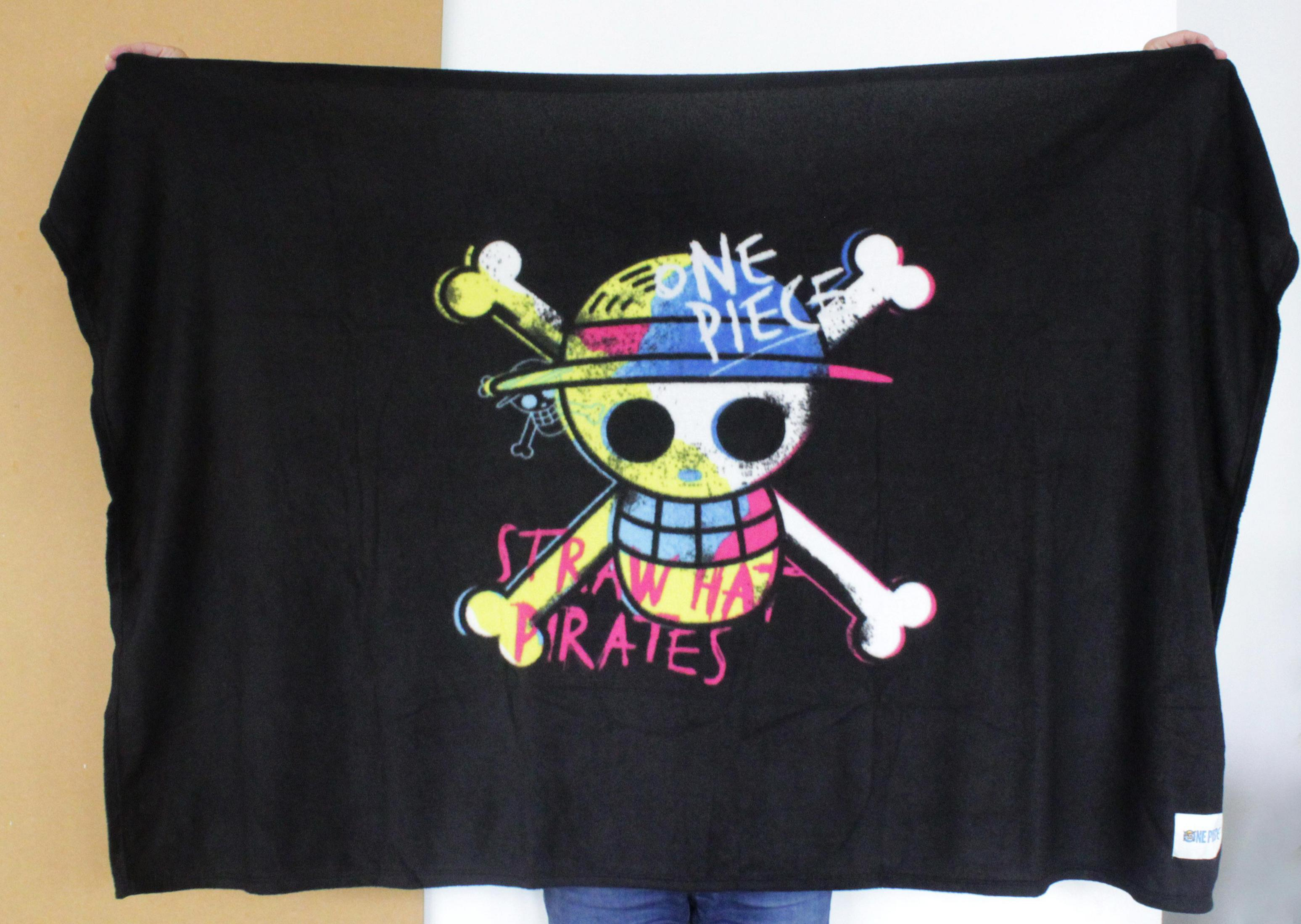 Eine Person hält eine große schwarze One Piece Decke mit einem Totenkopf- und Knochenmotiv.