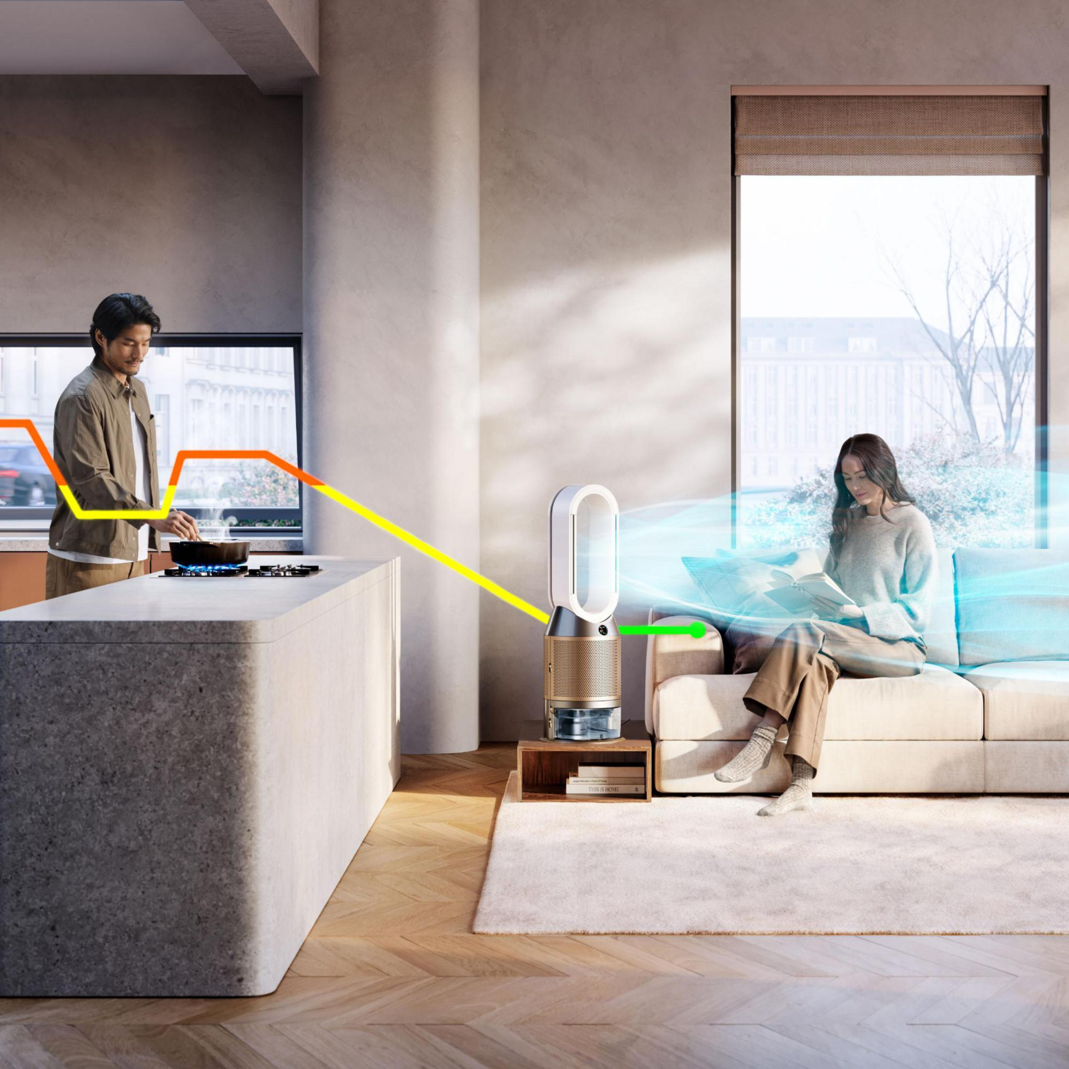 Szene einer Person, die in einer Küche kocht, mit einem Dyson-Luftreiniger zwischen ihr und einer anderen Person, die auf einer Couch liest.