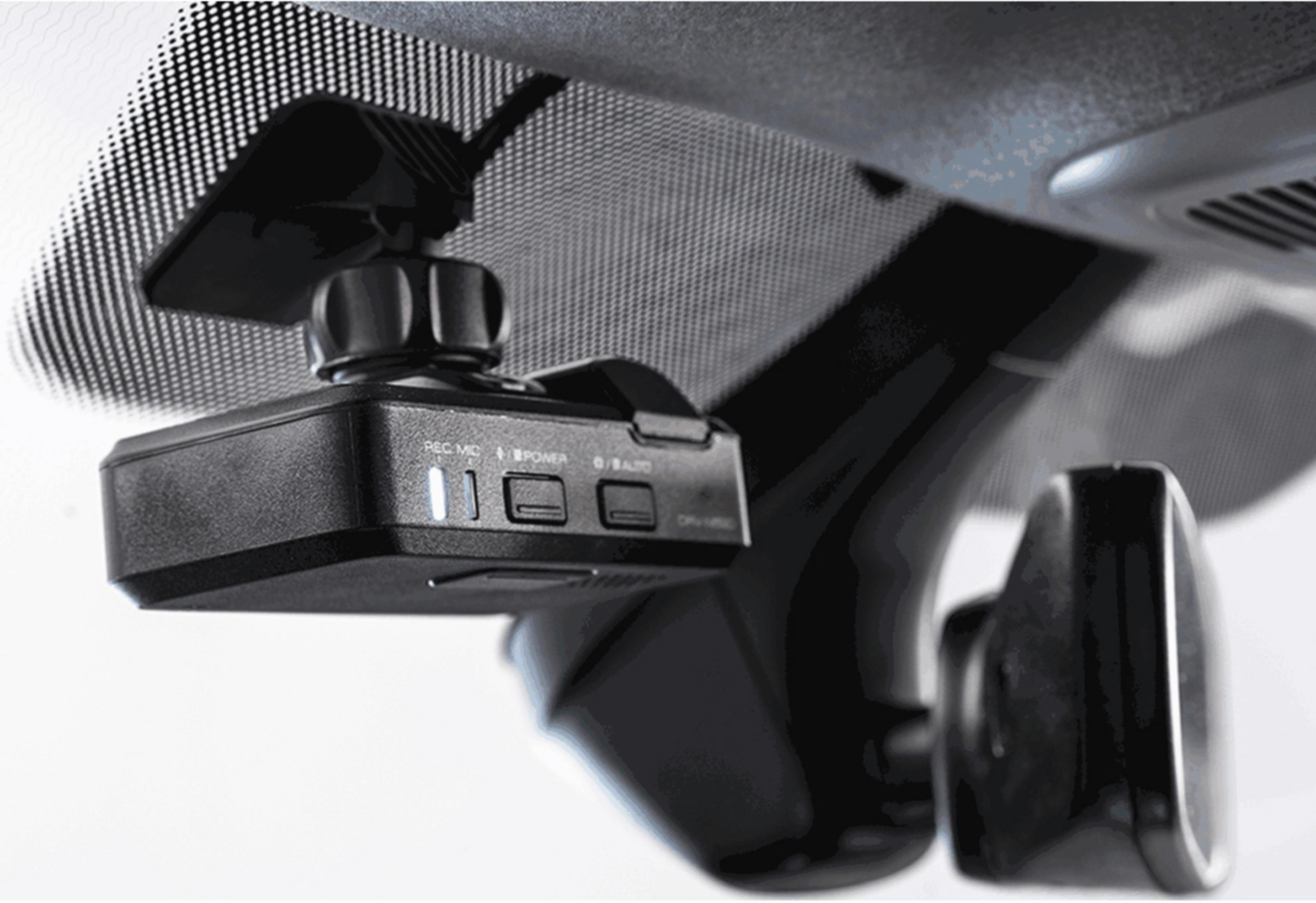 Una dashcam nera è montata sotto lo specchietto retrovisore di un'auto, con un parabrezza sullo sfondo.