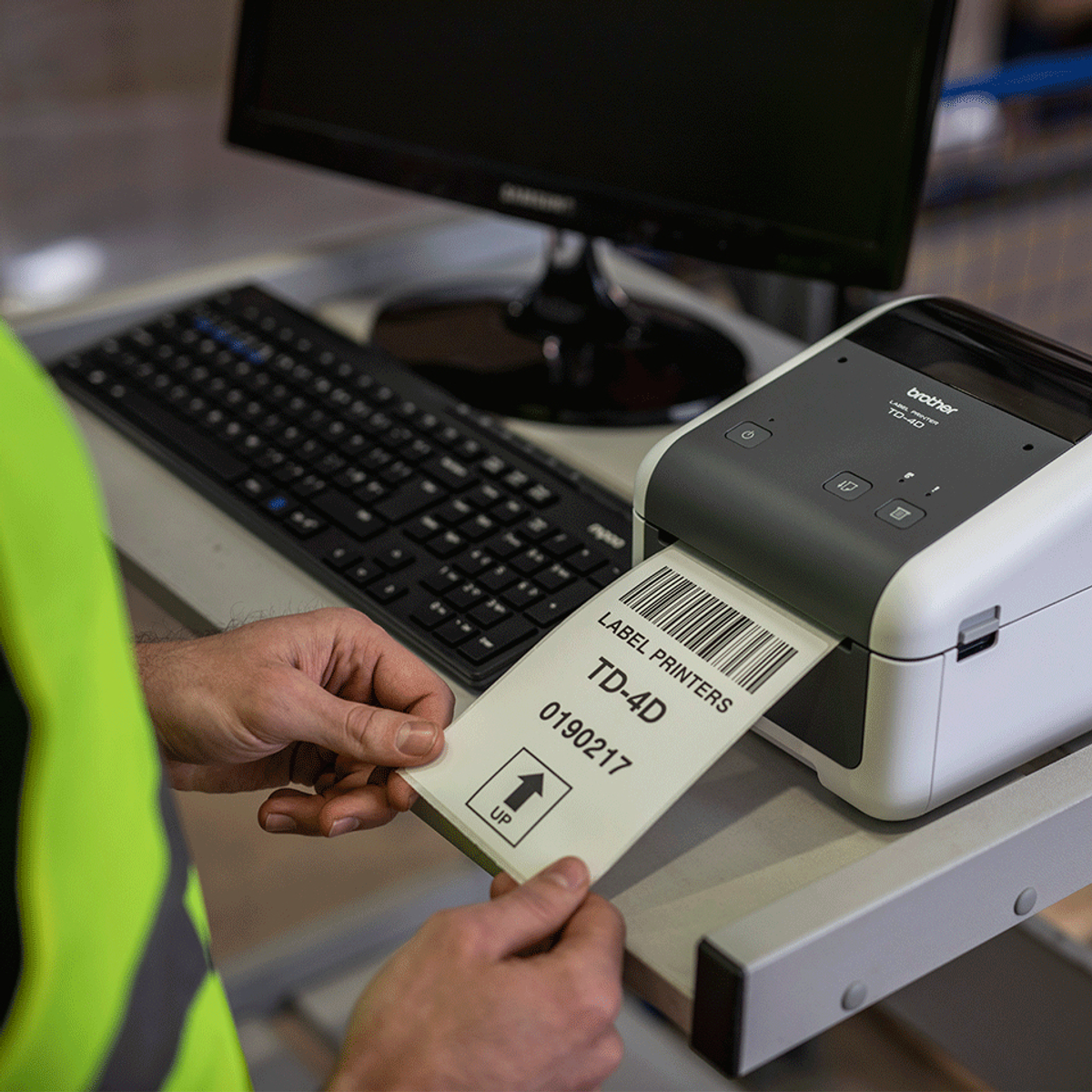 Osoba w kamizelce ochronnej trzyma wydrukowaną etykietę z drukarki Brother TD-4D w magazynie.
