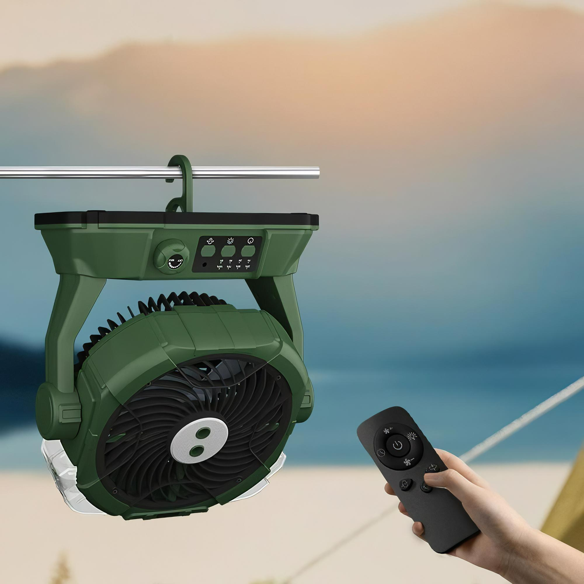 Grüner Campingventilator mit Lichtern hängt, Hand hält Fernbedienung. Die Lüfterflügel sind sichtbar.