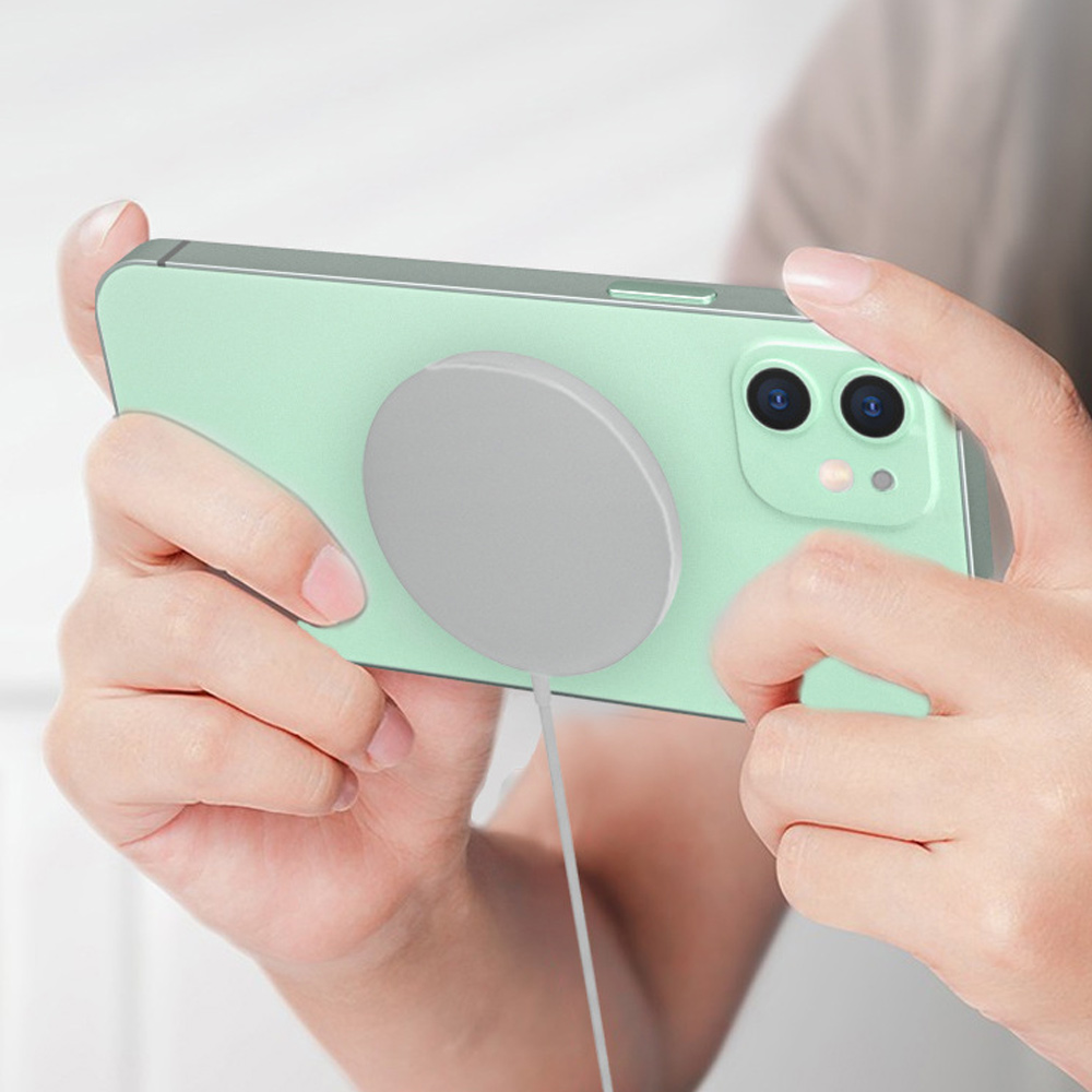 Hände halten ein hellgrünes Telefon, an dessen Rückseite ein graues kabelloses Ladegerät befestigt ist.