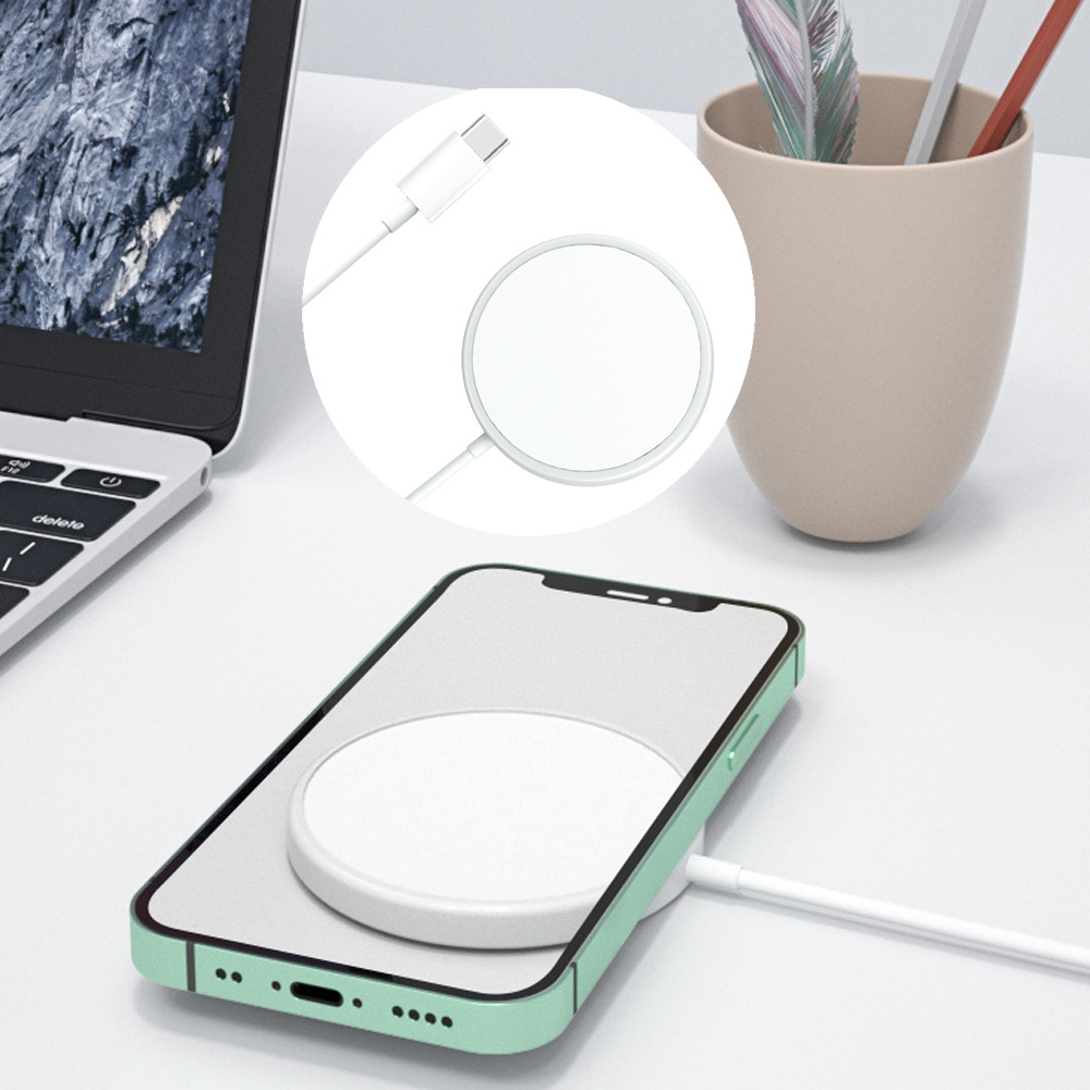Ein Telefon wird auf einem weißen kabellosen Ladegerät in der Nähe eines Laptops und einer Tasse mit Stiften auf einem weißen Tisch aufgeladen.