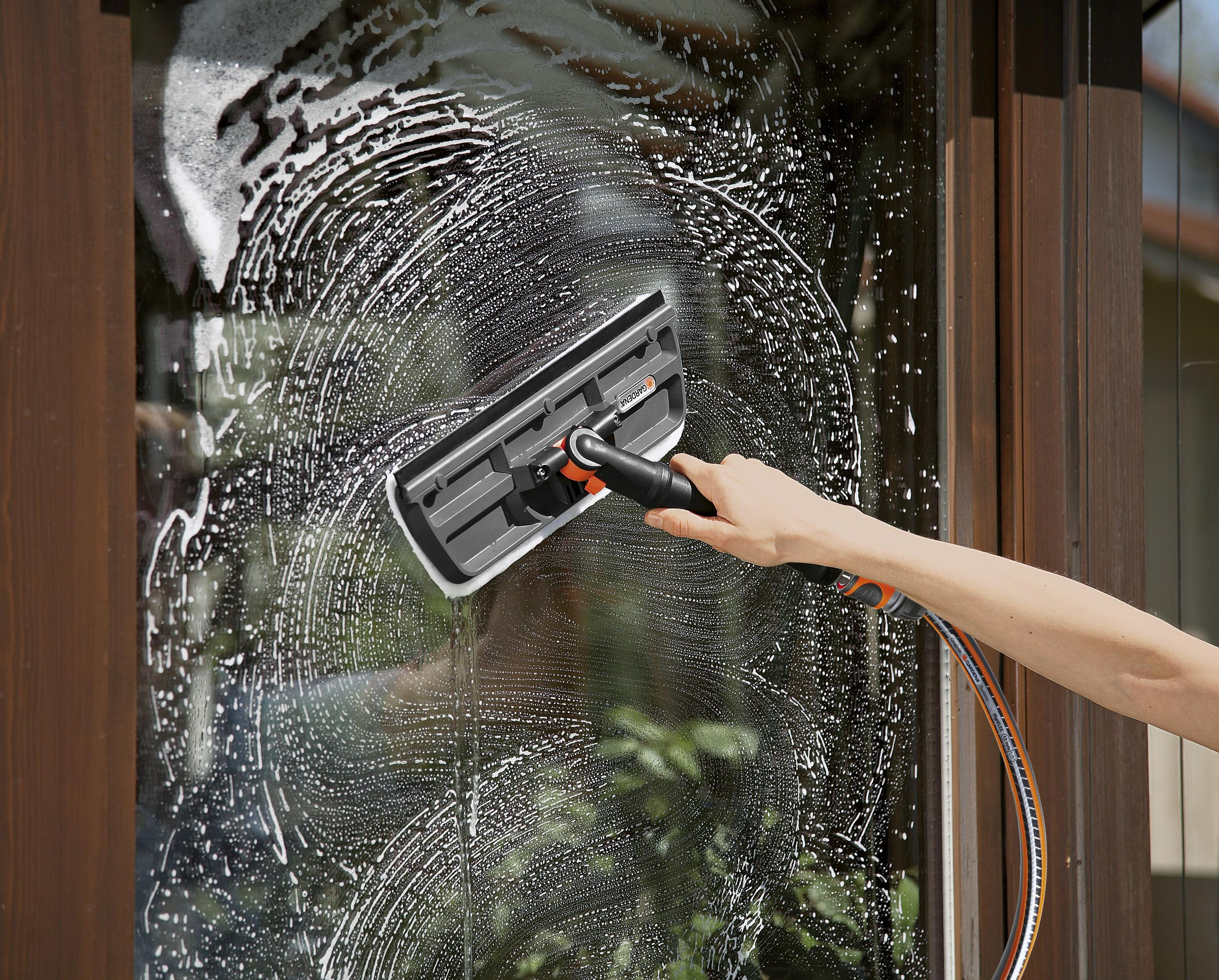 Hand hält Gardena-Reinigungswerkzeug und wäscht ein seifiges Fenster eines Gebäudes.