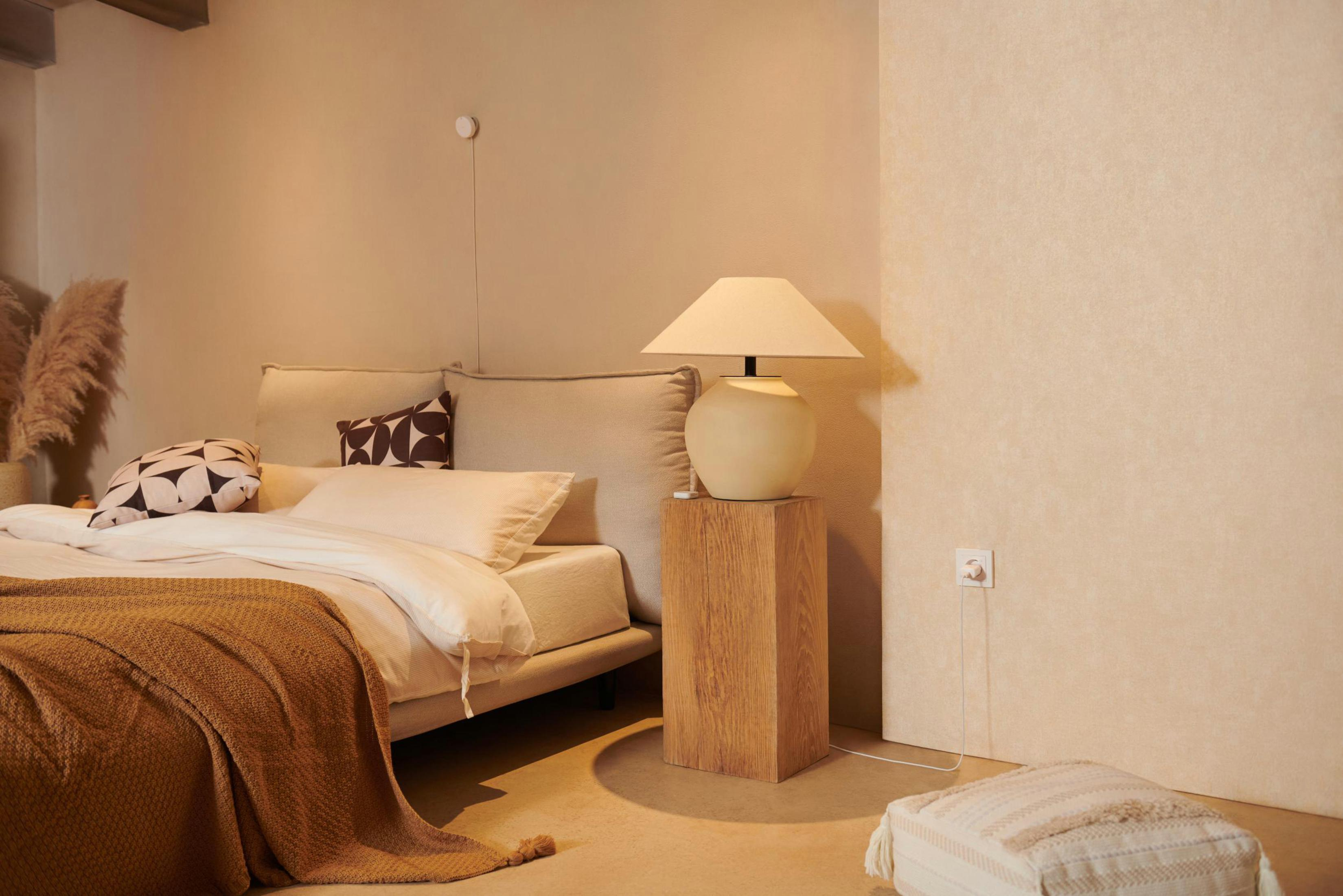 Schlafzimmerszene mit einem Bett, einer Lampe und einer Steckdose in Bodennähe.