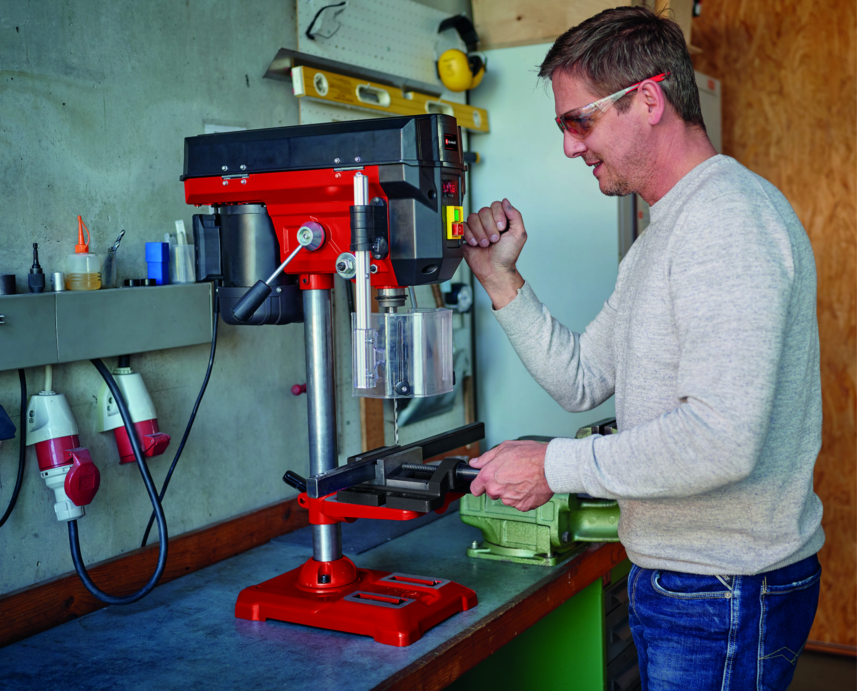 Mann bedient eine rot-schwarze Bohrmaschine in einer Werkstatt.