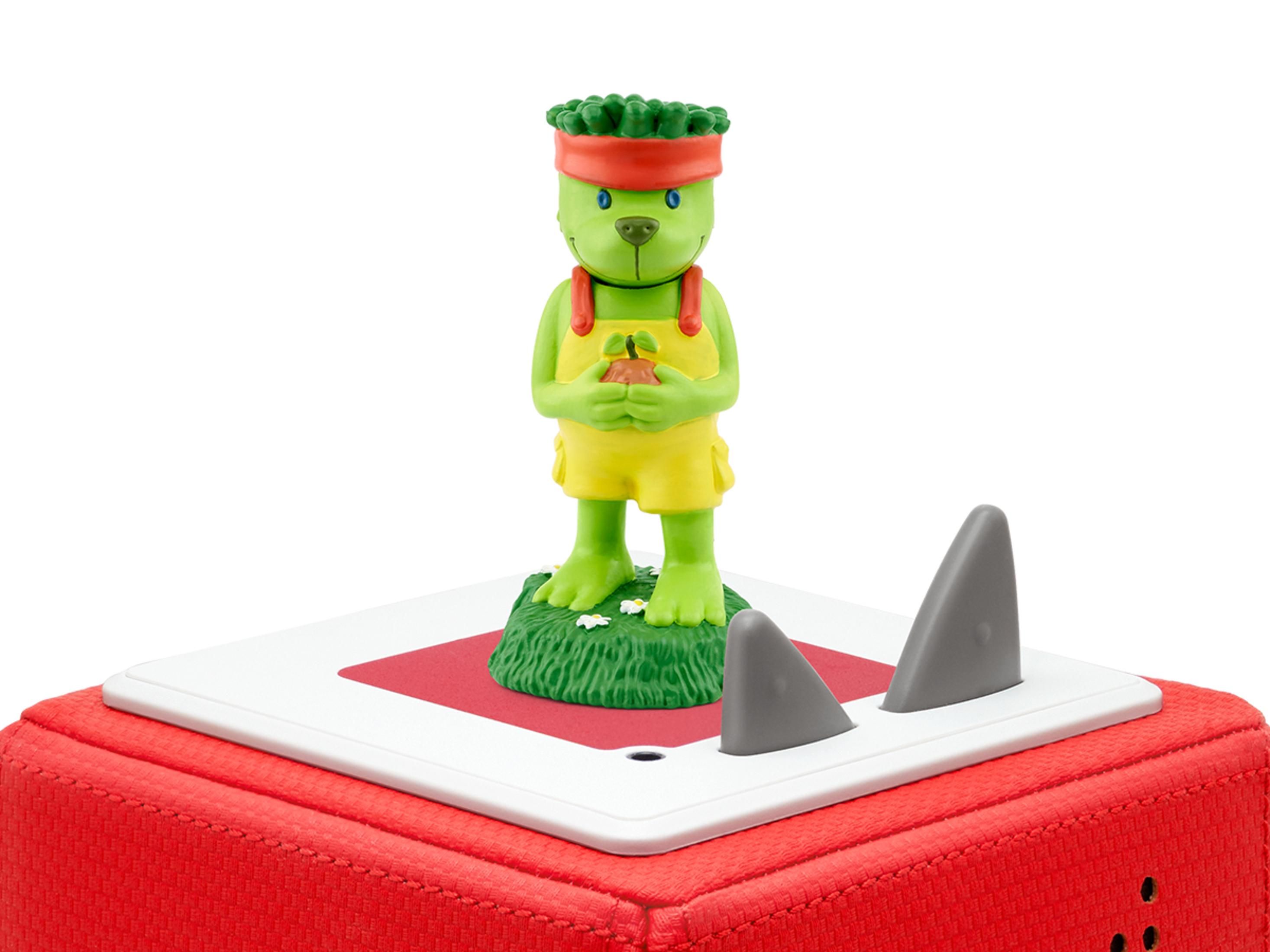 Eine grüne Figur in gelber Kleidung steht auf einem Lautsprecher mit haifischflossenförmigen Aufsätzen.