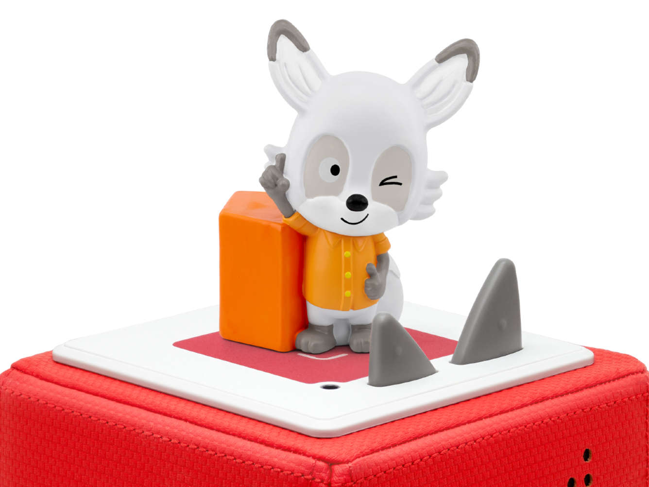 Un personnage jouet Lalalinos avec une chemise orange, des accents gris et un œil qui cligne se tient sur une boîte rouge et blanche.