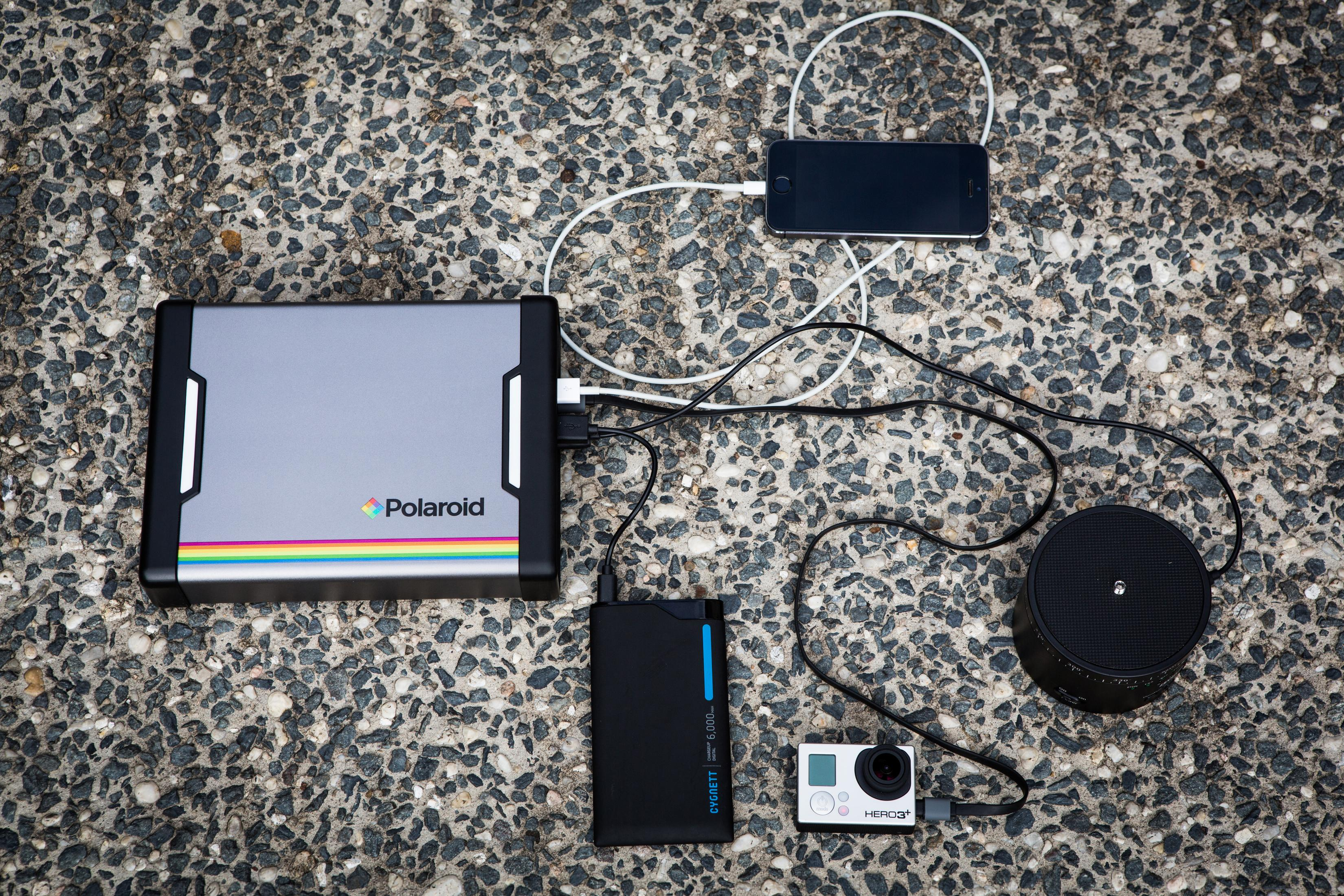 Power bank Polaroid con diversi dispositivi in carica su una superficie di cemento grigio.