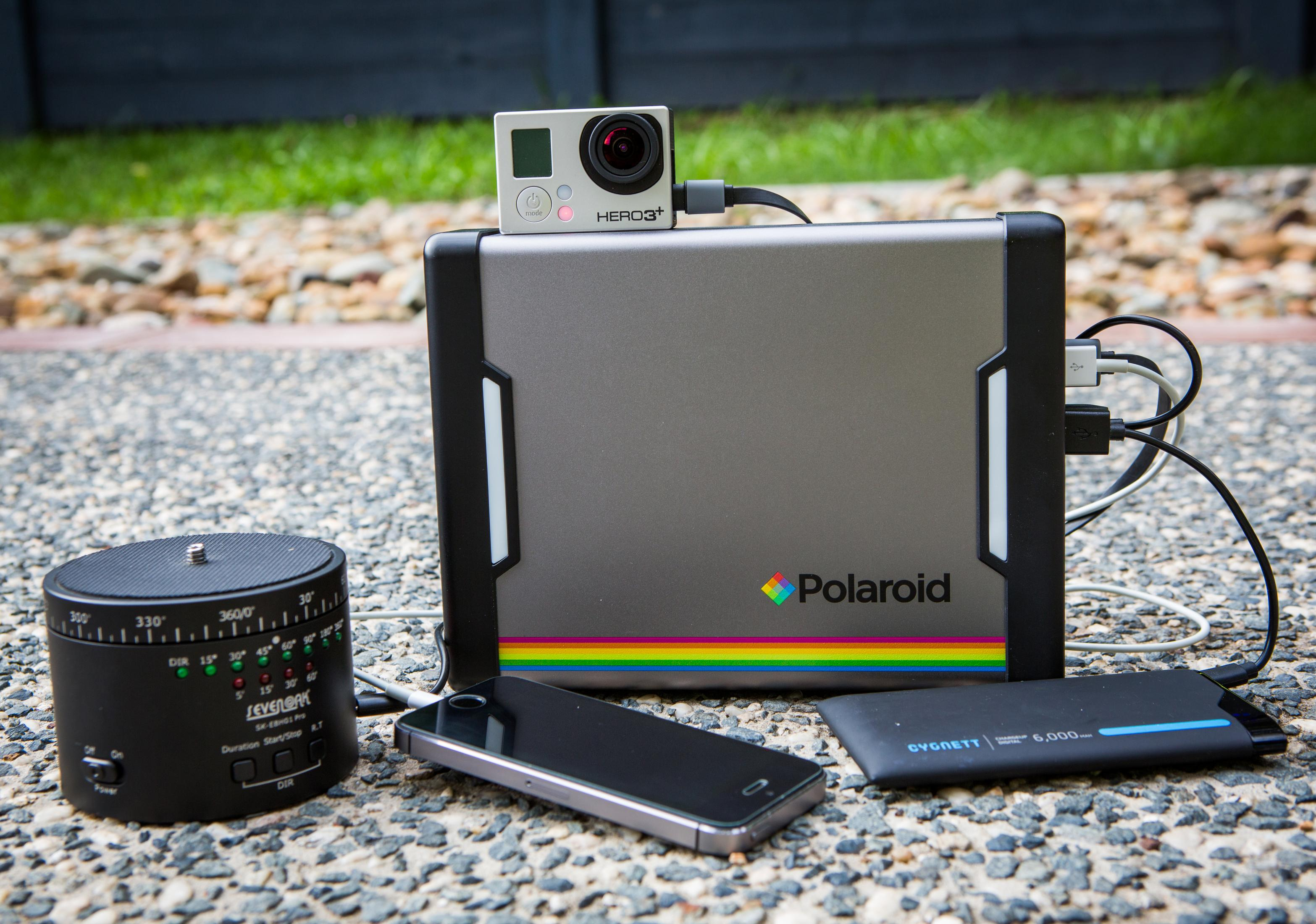 Power bank Polaroid che carica dispositivi su una superficie di ciottoli.