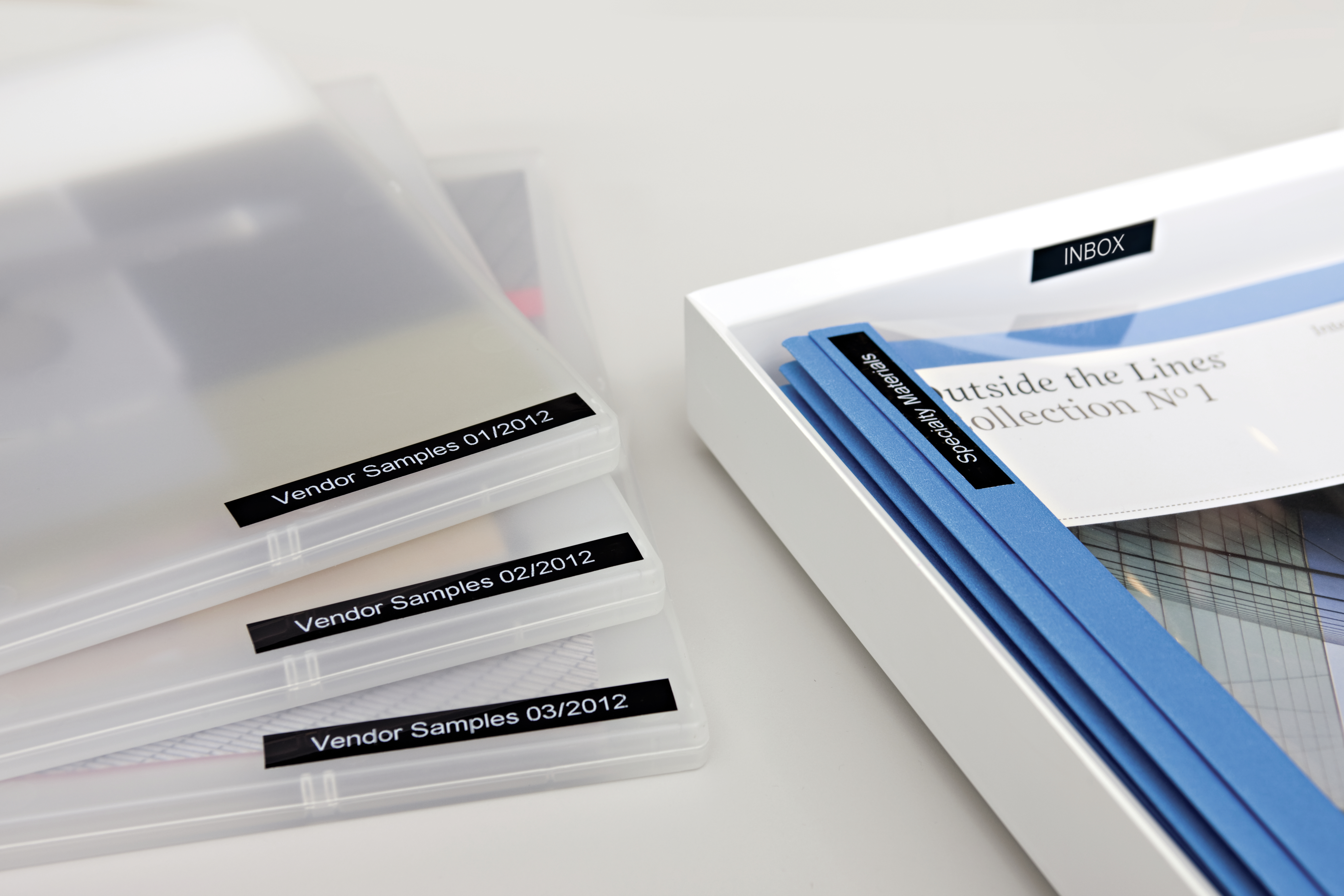 Pliki w przezroczystych etui, z etykietą 'Vendor Samples'. Niebieskie i białe pudełka z etykietami 'INBOX' i 'Outside the Lines'.