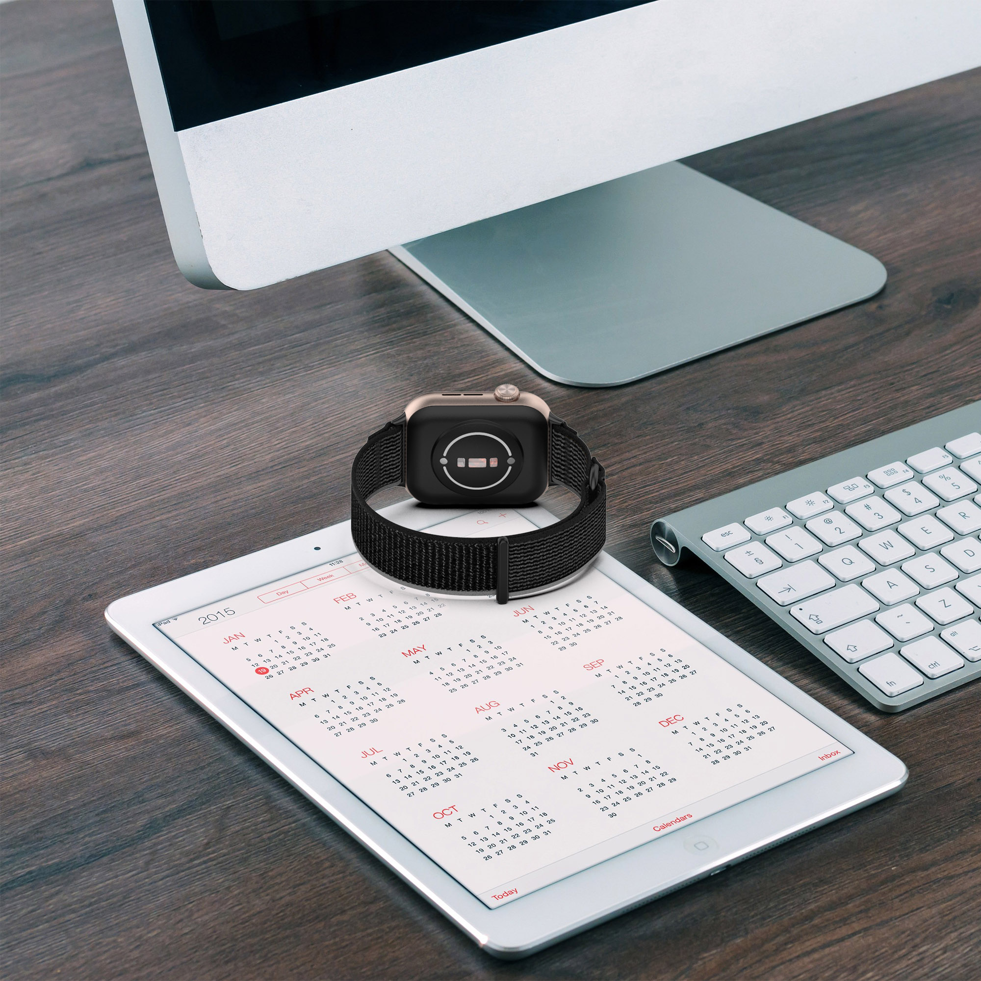 Smartwatch z czarnym paskiem leżący na tablecie, klawiaturze i monitorze komputera.