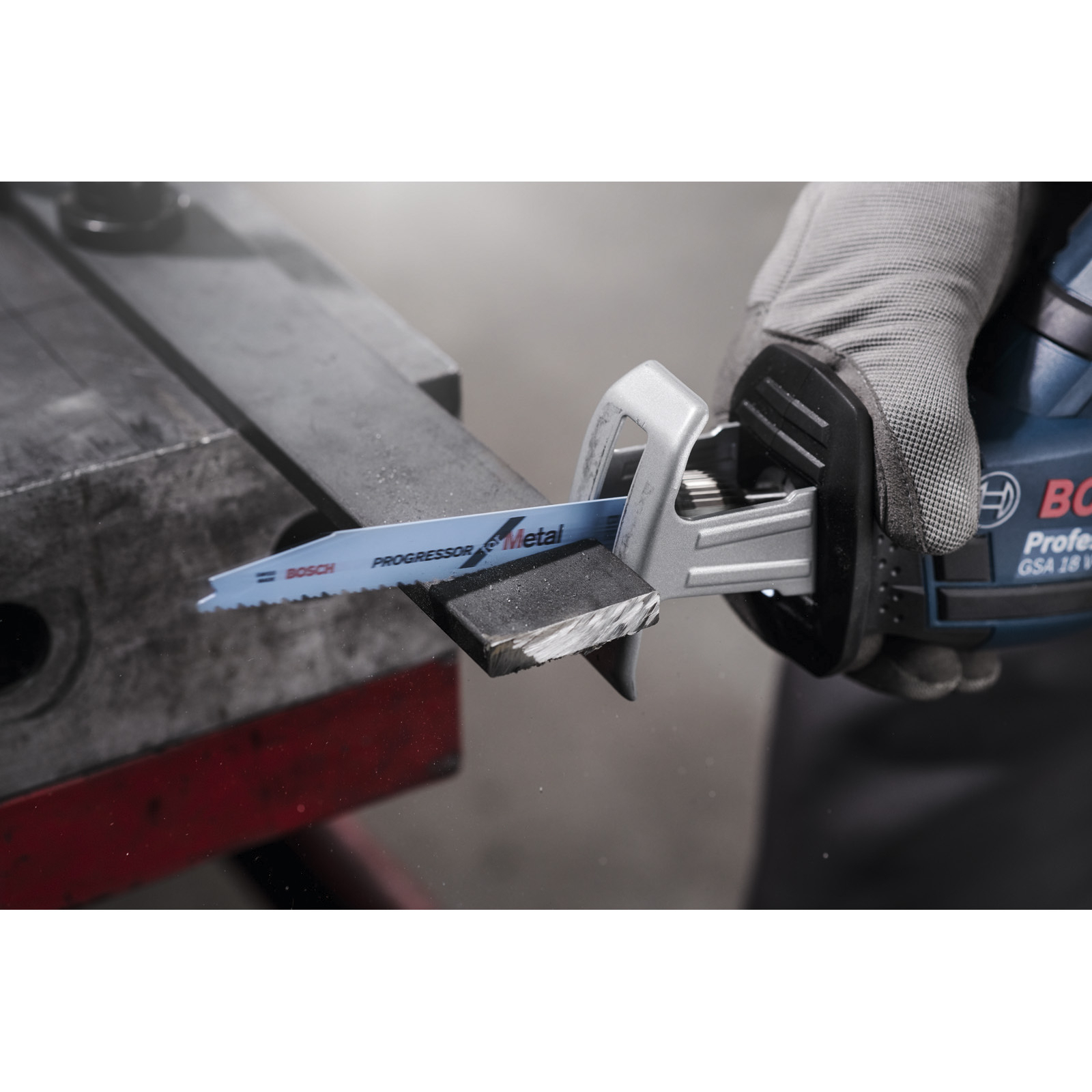 Ręka w rękawicy używa niebieskiej piły szablastej Bosch do cięcia kawałka drewna na metalowej powierzchni.