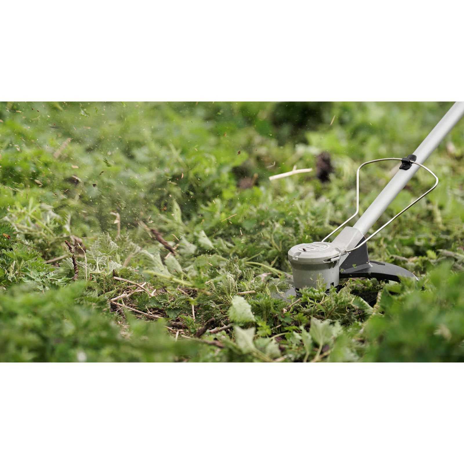 Zbliżenie na podkaszarkę w akcji, koszącą zieloną trawę z latającymi odłamkami.