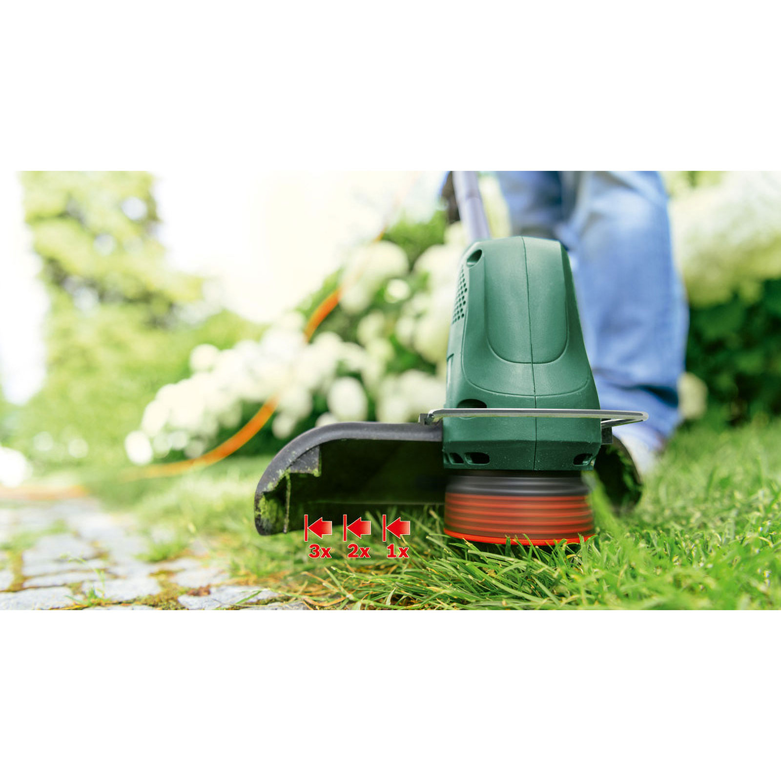 Gros plan d'un coupe-bordures vert coupant de l'herbe, montrant le mécanisme de coupe et les réglages de hauteur.