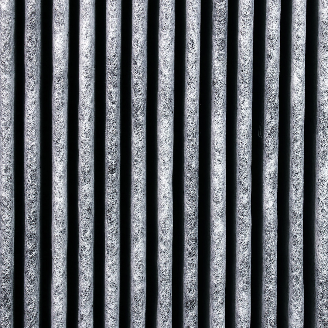 Nahaufnahme eines Aktivkohle-Luftfilters mit vertikalen, parallelen grauen Linien. Der Hintergrund ist schwarz.
