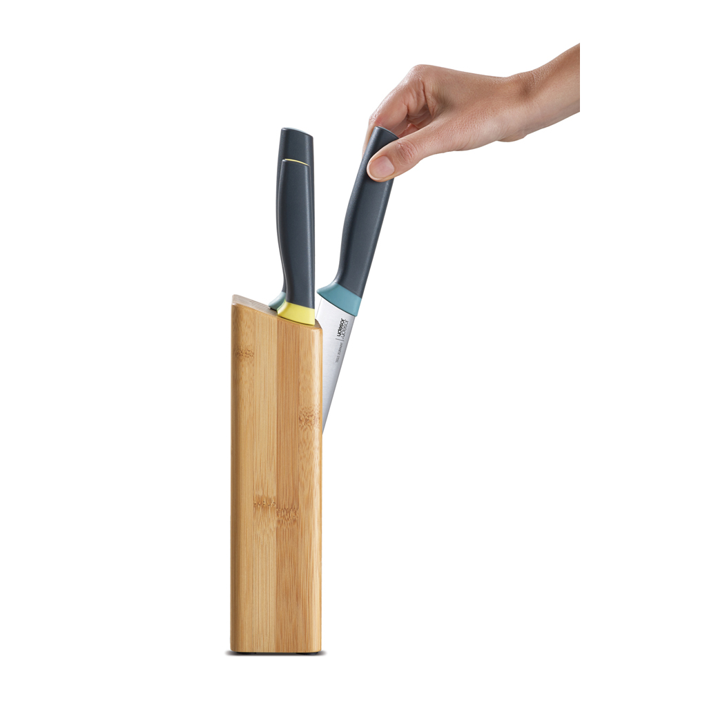 Una mano introduce un cuchillo en un bloque de cuchillos de madera. Mango negro.