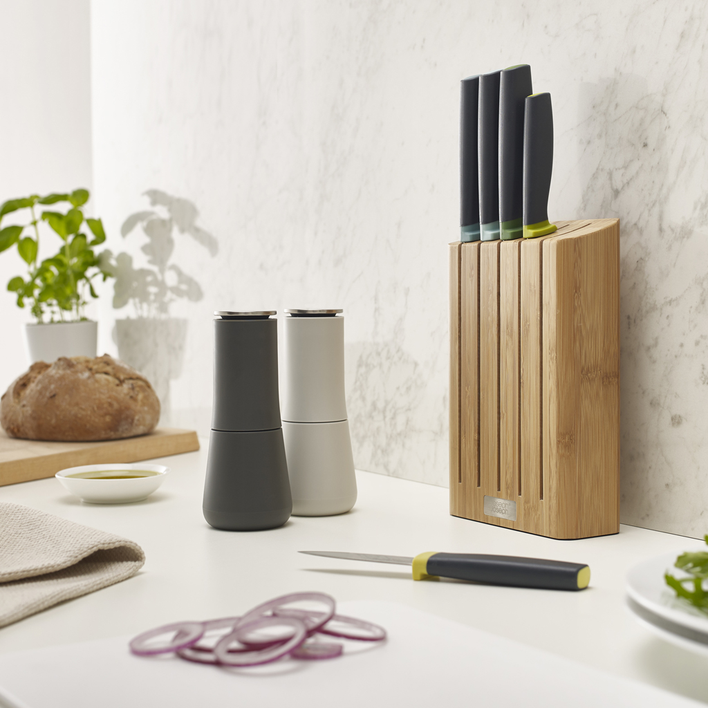 Escena de cocina con un bloque de cuchillos, cuchillos y otros utensilios. Encimera blanca.
