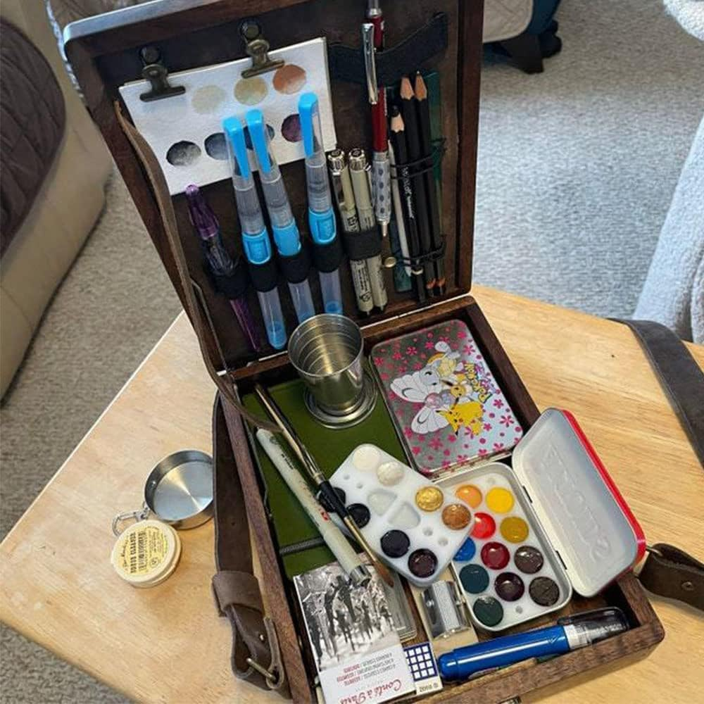 Die Kunstutensilien einer Person sind ordentlich in einer offenen Holzkiste auf einem Tisch organisiert.