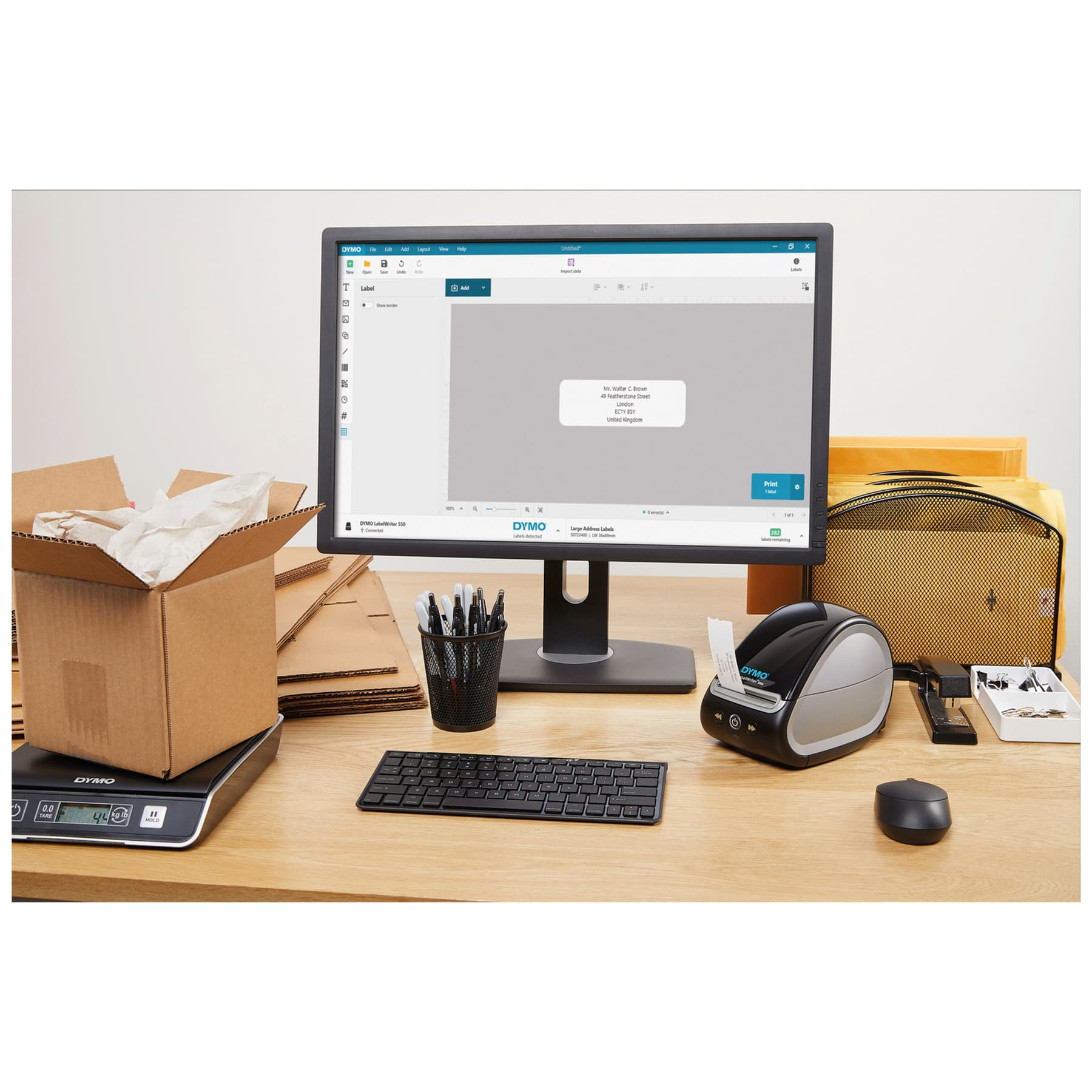 Un'impostazione da scrivania con un monitor, una stampante per etichette, una bilancia, una tastiera e altre forniture per ufficio.