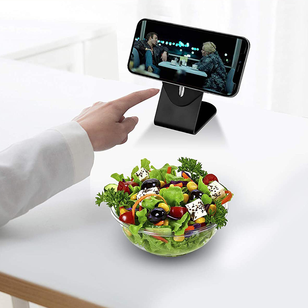 Telefon auf Ständer spielt Film ab, Hand zeigt auf Bildschirm, Salatschüssel auf Tisch, weißer Hintergrund.