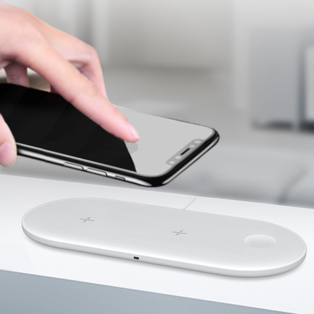 Eine Hand legt ein schwarzes Smartphone auf ein weißes kabelloses Ladepad auf einem weißen Tisch.