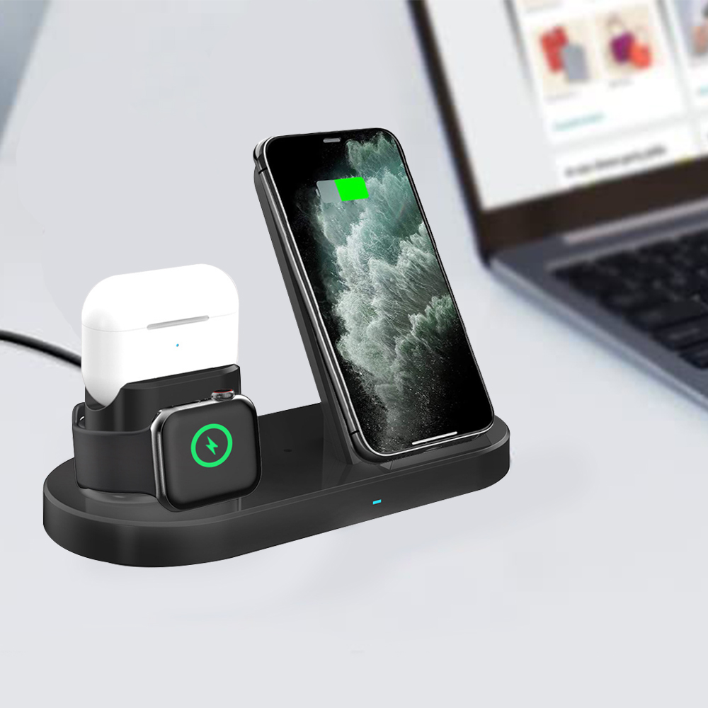 Eine schwarze Ladestation lädt ein Telefon, eine Uhr und Ohrhörer auf, vor dem Hintergrund eines Laptops in einer hellen Szene.