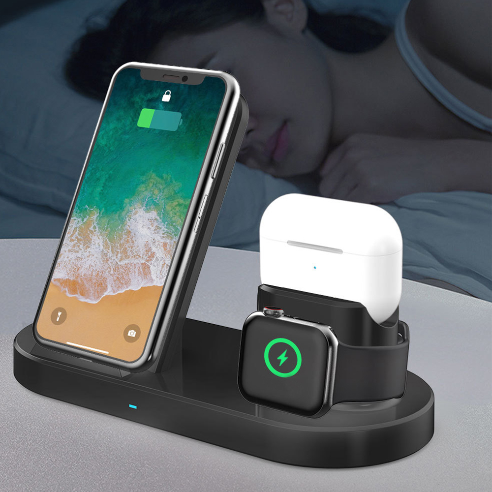 Eine schwarze Ladestation lädt ein Telefon, eine Uhr und Ohrhörer neben einer schlafenden Person in einem schwach beleuchteten Raum auf.
