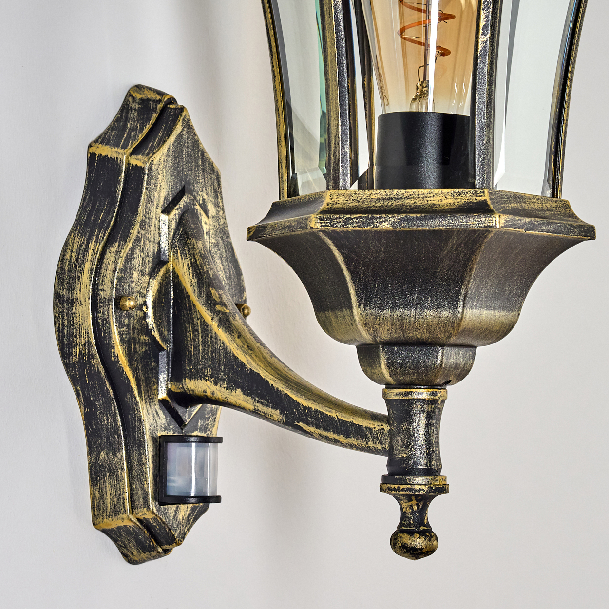 Eine Nahaufnahme einer bronzefarbenen Außenwandleuchte mit klarem Glas und einem Bewegungssensor.