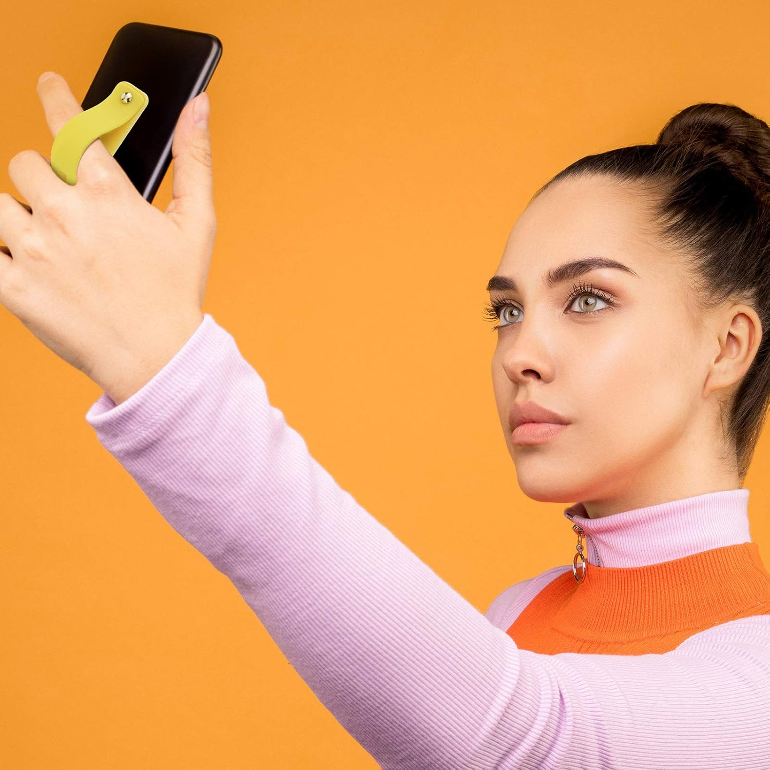 Eine Frau in einem lavendelfarbenen Oberteil mit orangefarbenem Kragen hält ein schwarzes Telefon mit einem lindgrünen Griff.