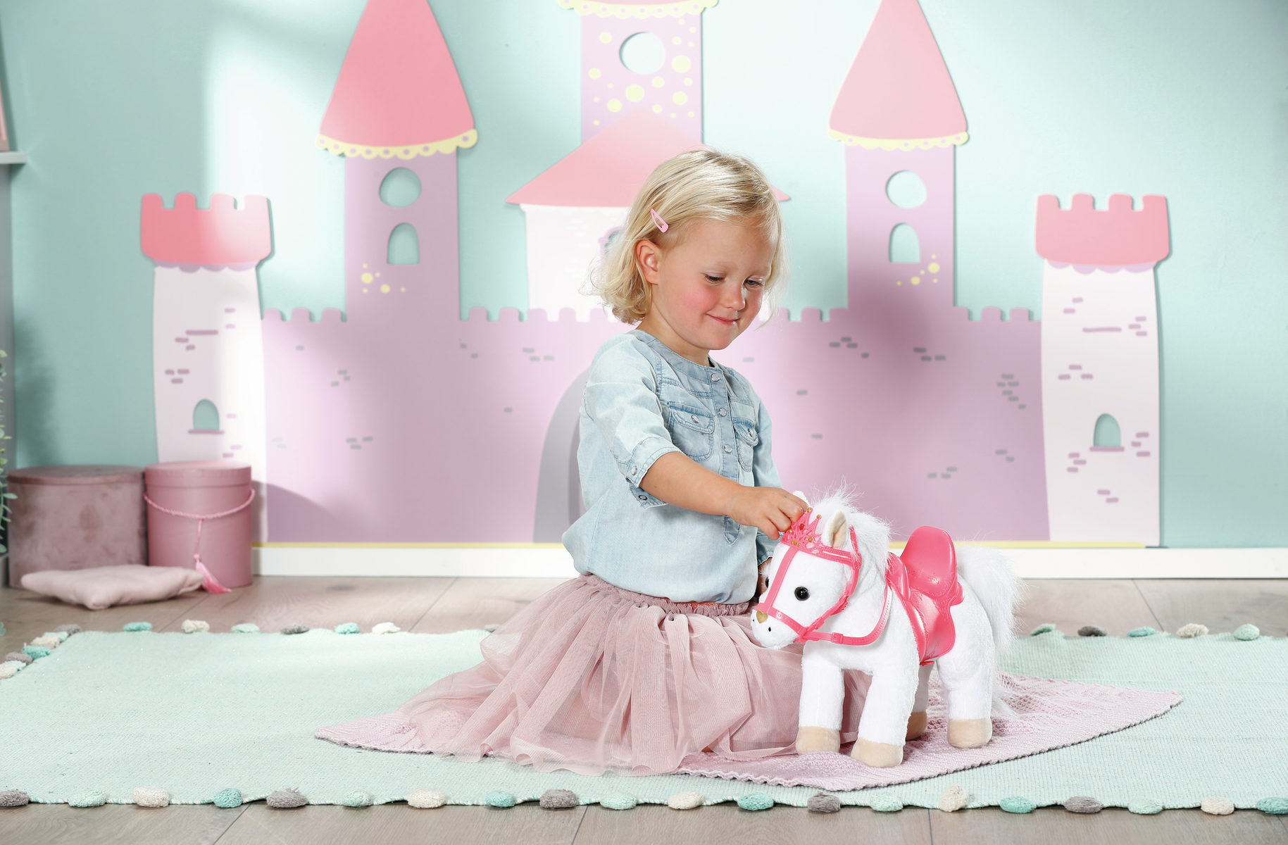 Ein Mädchen mit einem Spielzeugpferd. Das Pferd ist weiß mit rosa Sattel und Krone. Hintergrund ist ein Schloss.