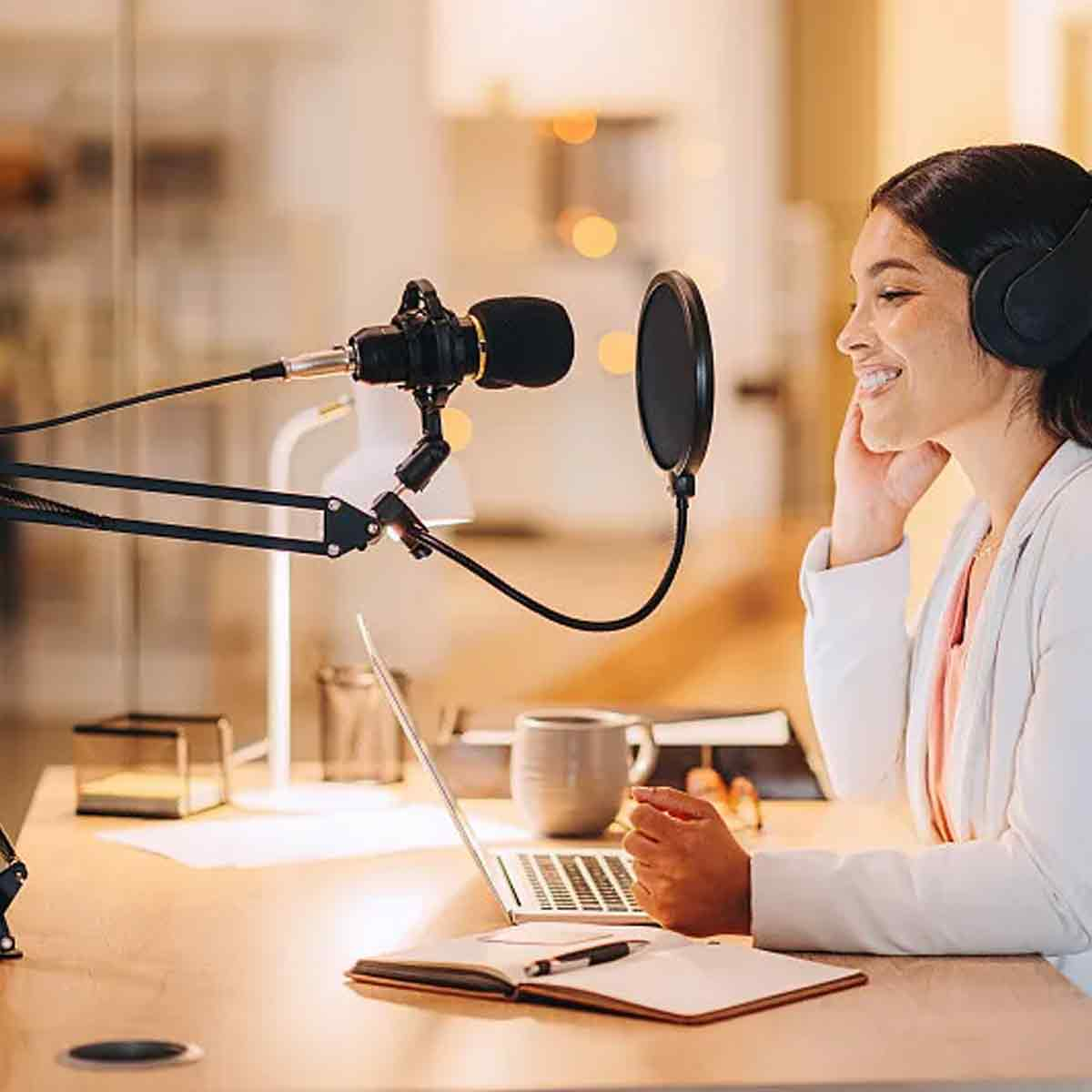 Eine Frau nimmt in einem hellen, modernen Studio einen Podcast mit Mikrofon, Laptop und Kopfhörer auf.