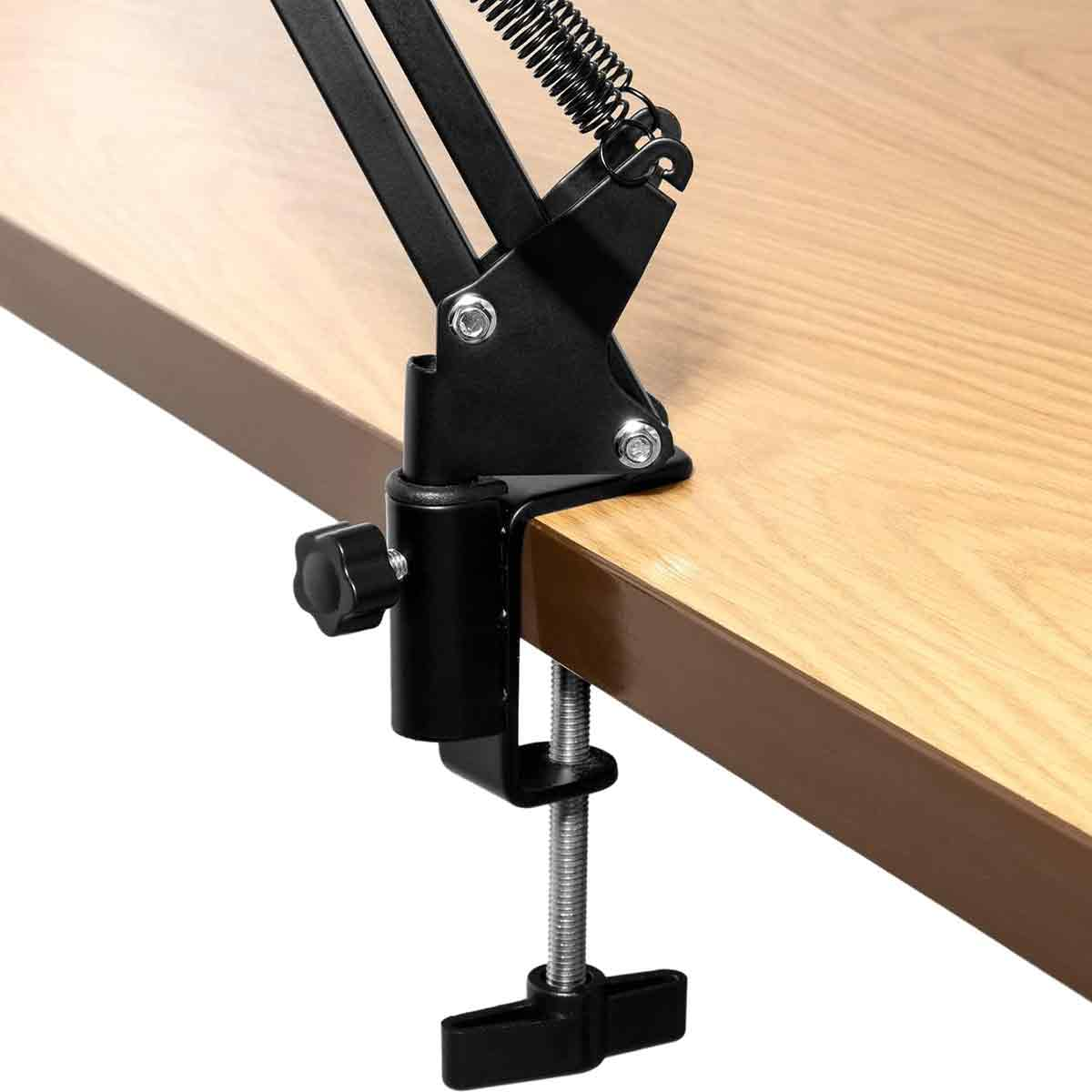 Eine schwarze Mikrofonständerklemme ist an einem hellbraunen Holzschreibtisch befestigt und zeigt den Befestigungsmechanismus.