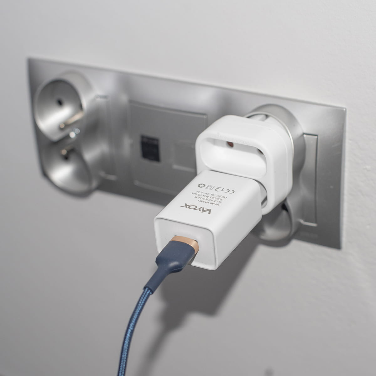 Podwójna wtyczka adaptera z ładowarką jest podłączona do gniazdka ściennego, z niebieskim kablem podłączonym do ładowarki.