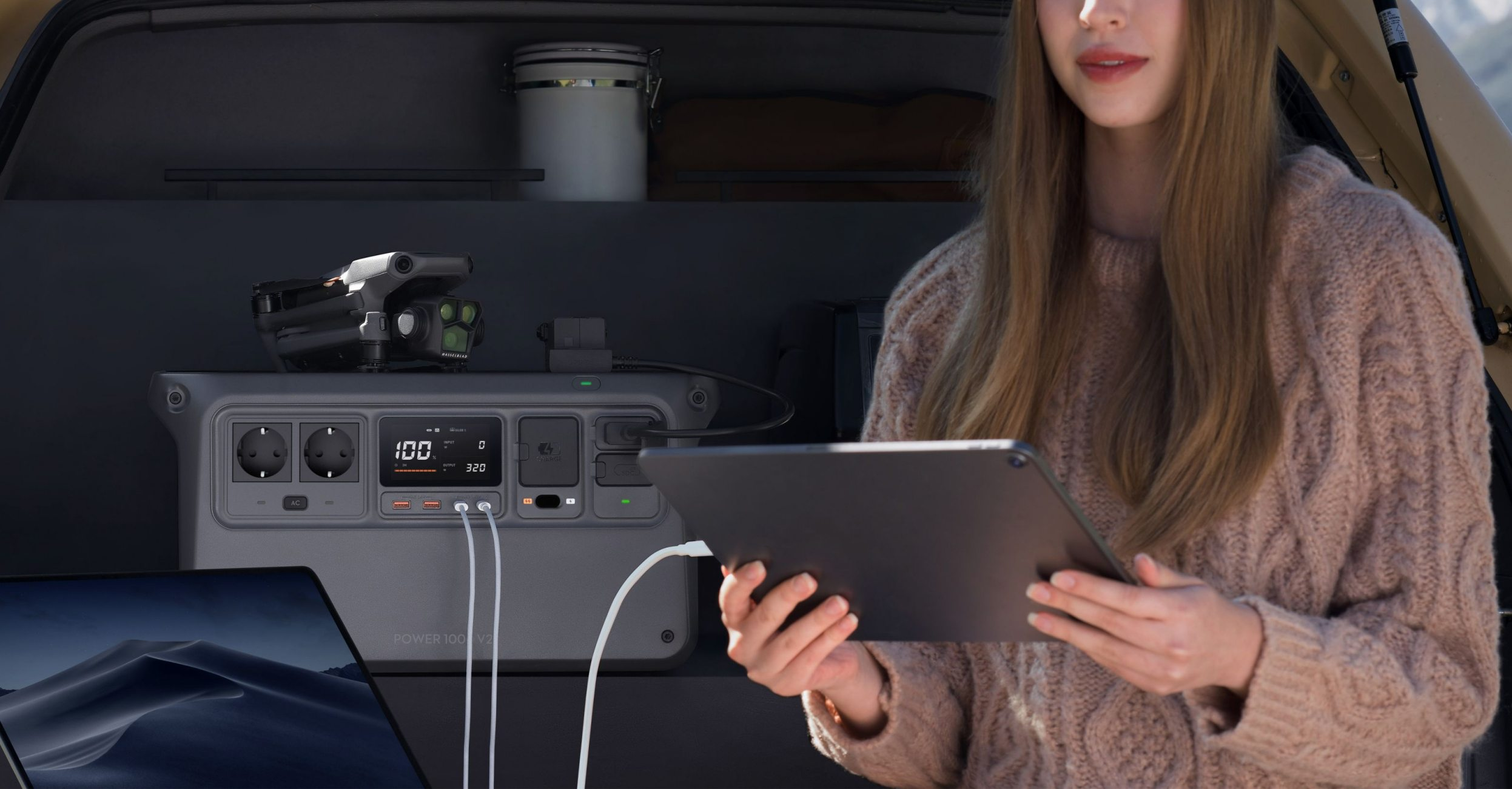 Eine Frau benutzt ein Tablet mit einer Powerstation, einem Laptop und einer Drohne in einem Fahrzeug.