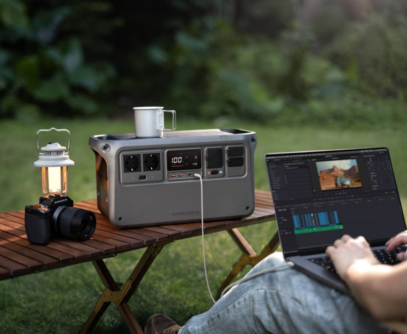 Eine Person benutzt einen Laptop mit einer Powerstation, einer Kamera und einer Laterne auf einem Tisch im Freien.