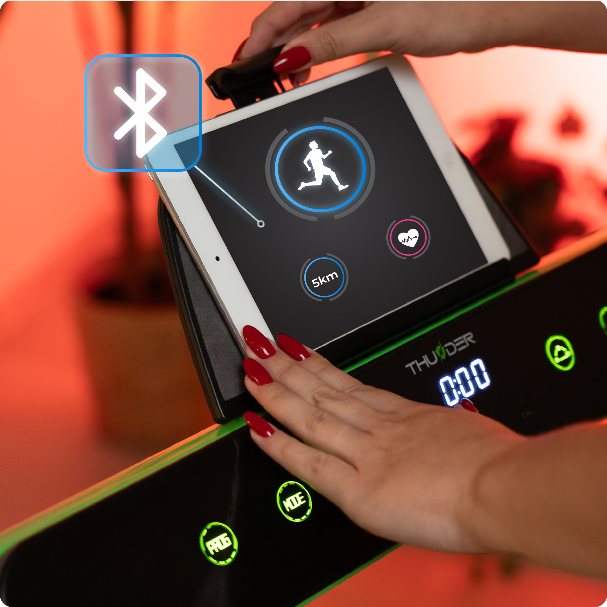 Zbliżenie dłoni wchodzących w interakcję z tabletem na bieżni. Widoczna ikona Bluetooth.