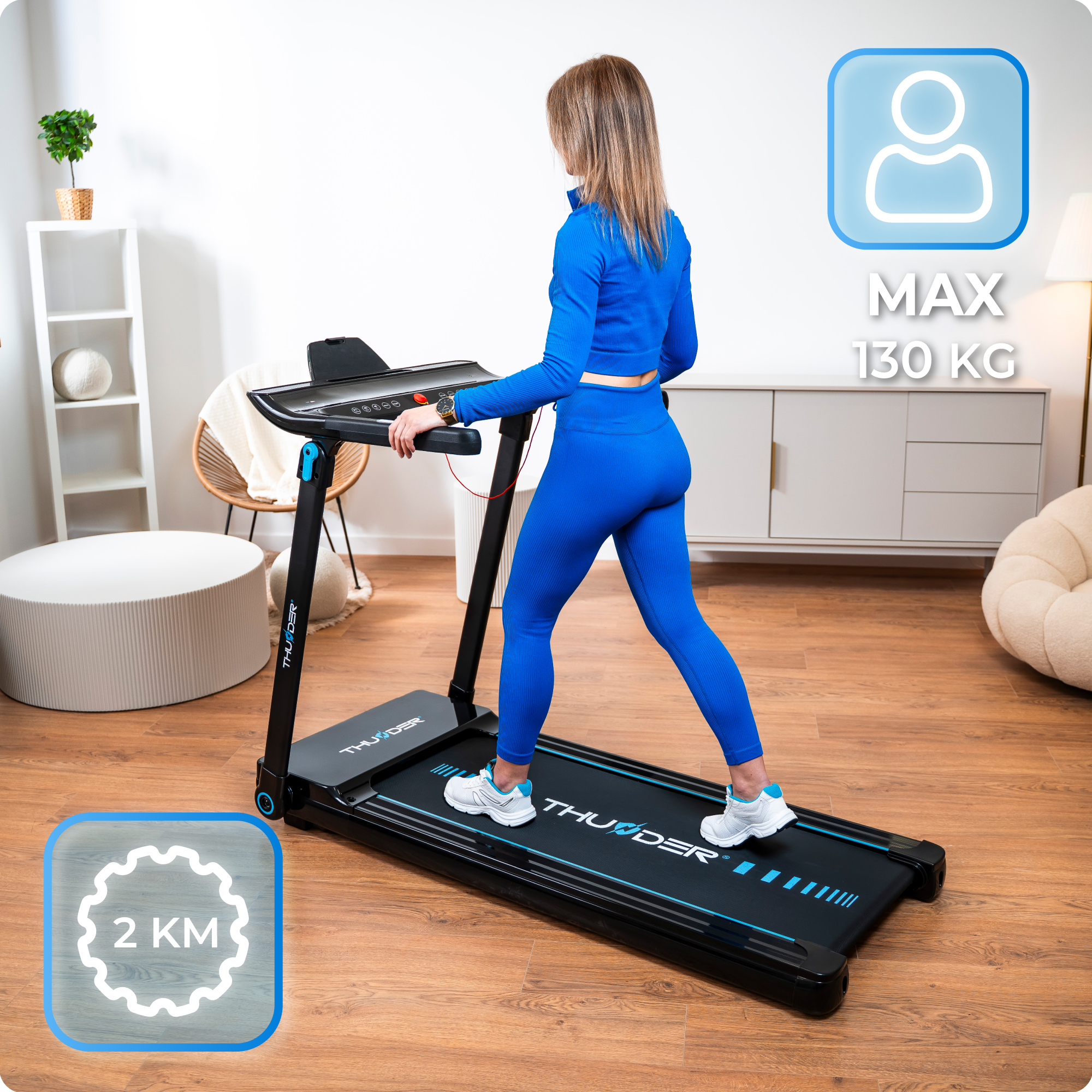 Kobieta chodzi po czarnej bieżni z niebieskimi akcentami, o maksymalnej wadze 130 kg i znaczniku odległości 2 km.